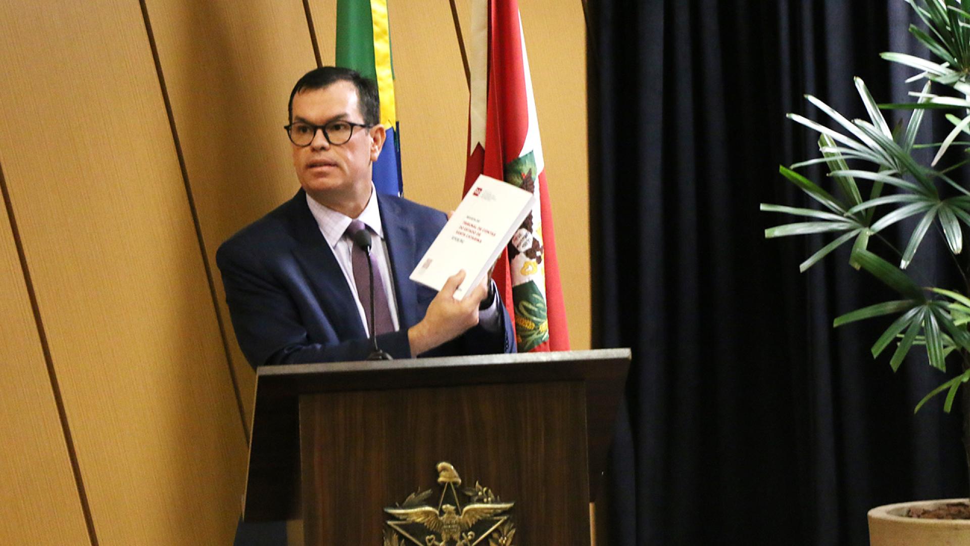 Foto do conselheiro Adircélio de Moraes Ferreira Júnior, presidente do Conselho Editorial da Revista do TCE/SC, no púlpito, mostrando a capa do periódico.