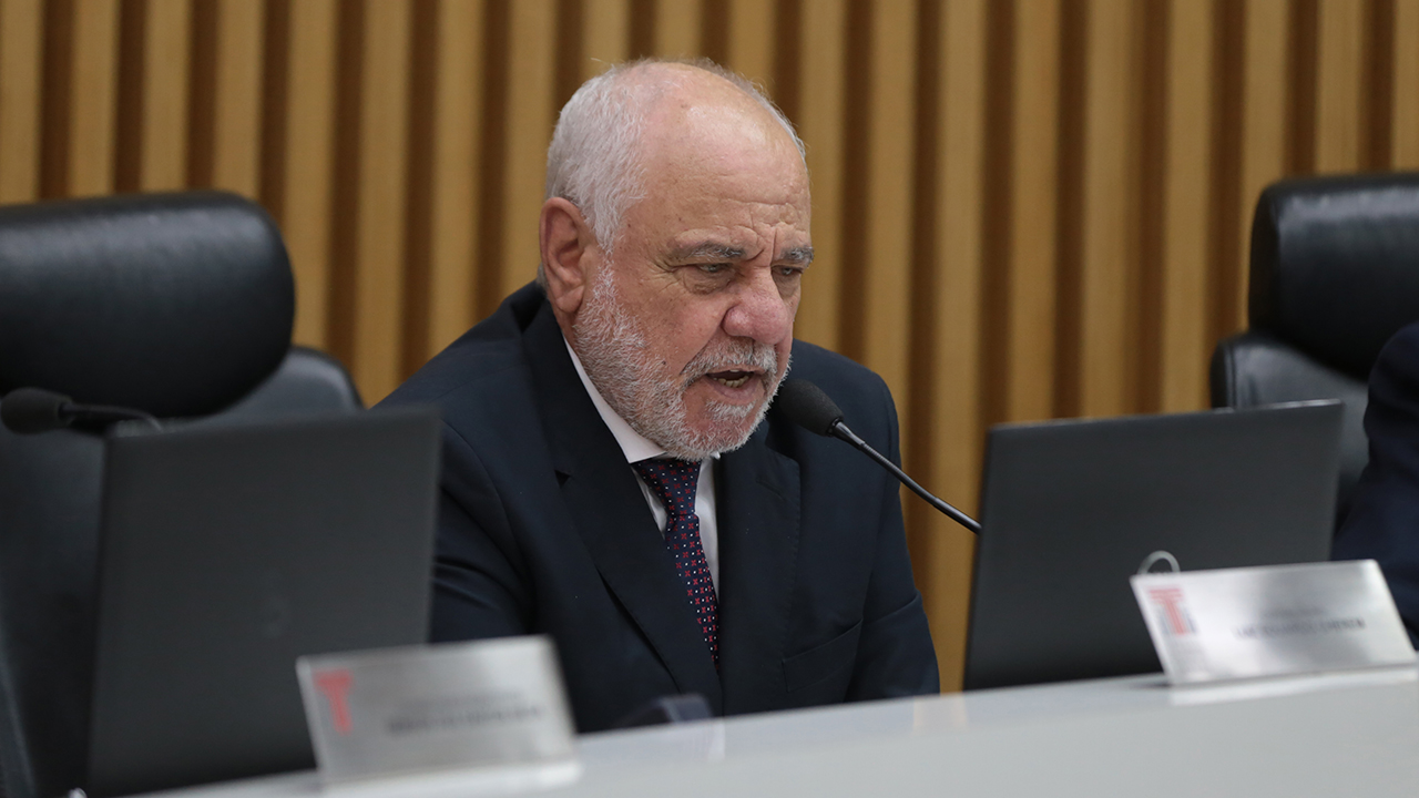 Foto do relator das contas do Governo do exercício de 2024, conselheiro Luiz Eduardo Cherem, durante sessão do Pleno. Ele é um homem branco, de cabelos e barba grisalhos. Está falando ao microfone, sentado em poltrona diante da bancada circular de autoridades que compõem o Plenário.