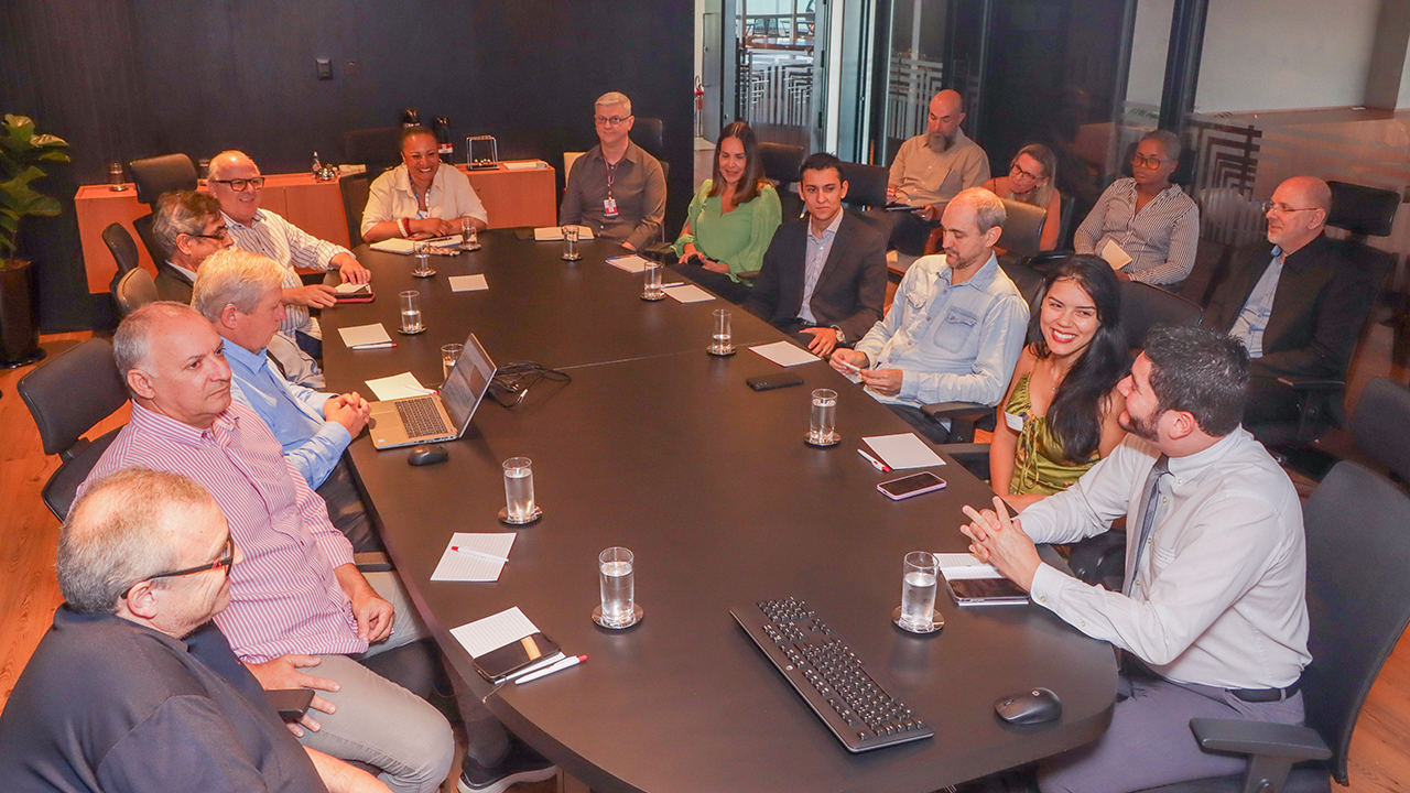 Foto horizontal com o conselheiro Wilson Wan-Dall e com servidores do TCE/SC e do TCE/PR — ao todo, há 16 pessoas, sendo 5 mulheres e 11 homens. A maioria está sentada em volta de uma mesa de reuniões. Sobre a mesa, há copos, papéis, canetas e equipamentos de informática. 