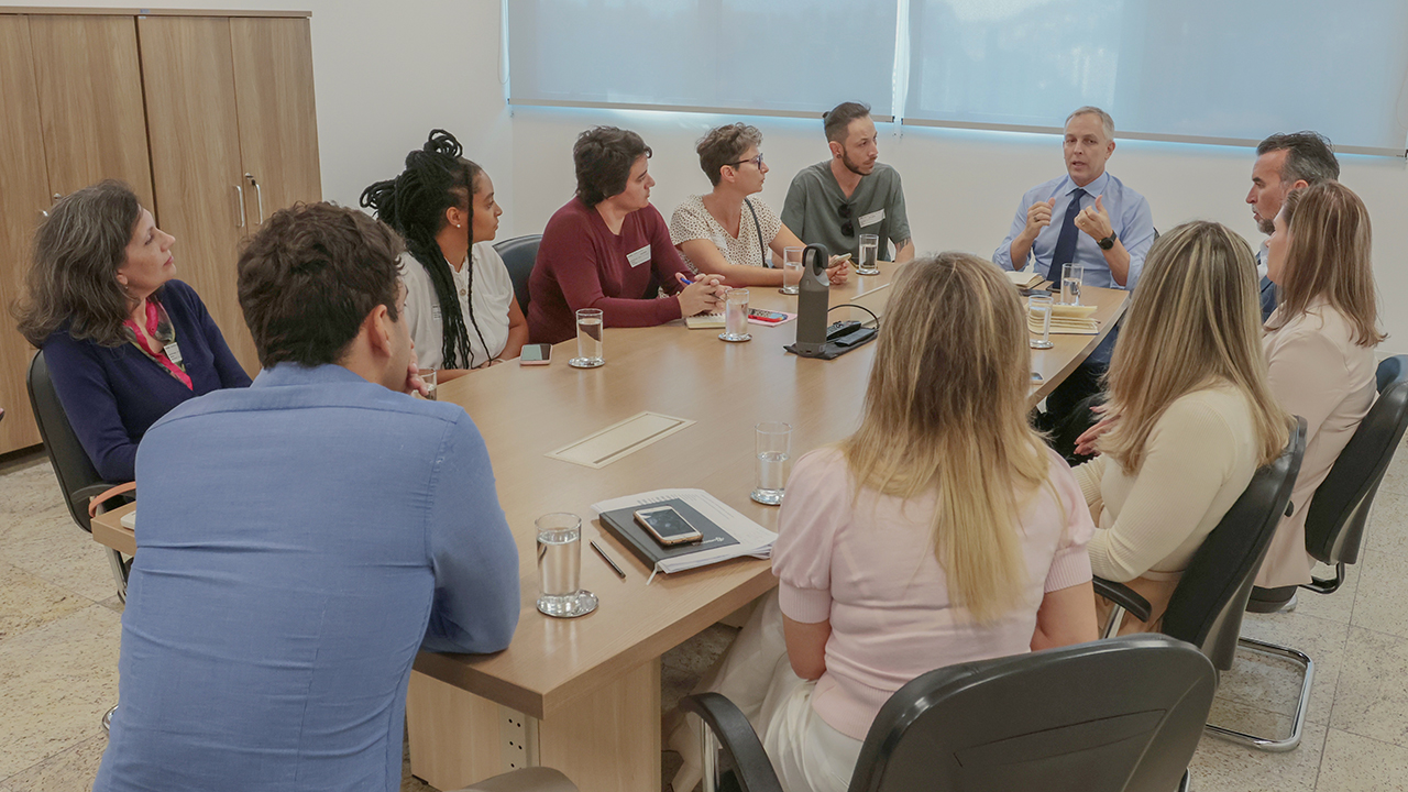 Foto do encontro realizado no TCE/SC. Há onze pessoas sentadas ao redor de uma mesa, entre homens e mulheres, enquanto conversam. Entre elas, estão representantes do Tribunal e do Conselho Municipal de Política Cultural de Florianópolis. Sobre a mesa, há papéis, cadernos, copos e canetas. 