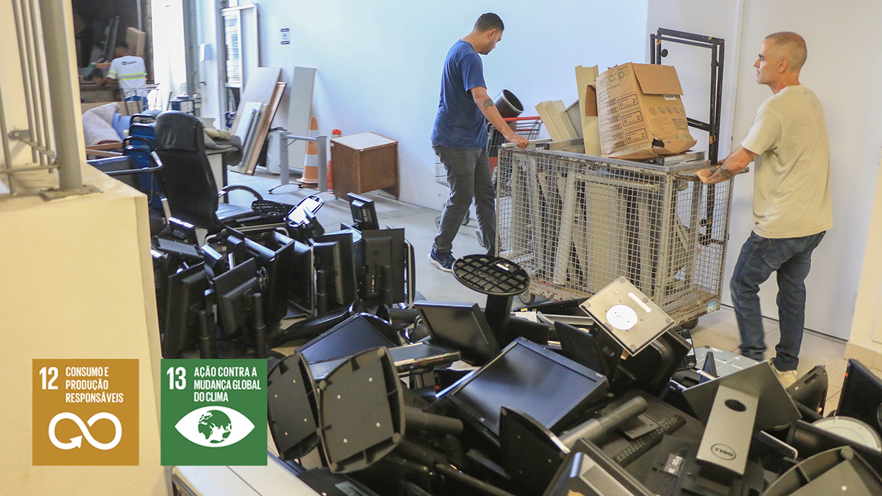 Banner horizontal com foto de dois homens carregando, em uma estrutura de ferro, móveis, eletrodomésticos e equipamentos de informática fora de condições de uso. Ao lado deles, há uma pilha de equipamentos eletrônicos para descarte. Sobre a imagem, no canto inferior esquerdo, os ícones dos Objetivos de Desenvolvimento Sustentável 12, consumo e produção responsáveis, e 13, ação contra a mudança global do clima. 