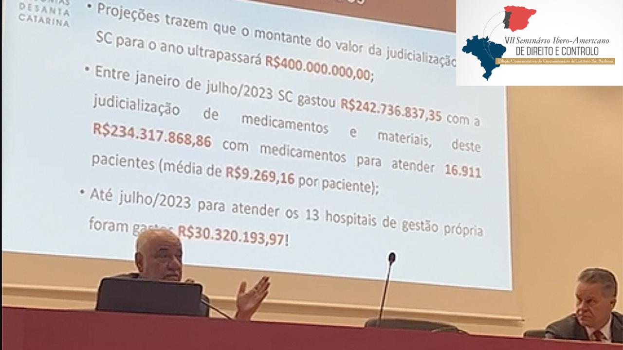 Foto do conselheiro Luiz Eduardo Cherem, sentado diante da bancada, palestrando no evento. Ao fundo, imagem de projeção da apresentação em PowerPoint. No canto superior direito, o logo do evento, com fundo branco e mapas do Brasil e da península Ibérica (Portugal e Espanha), unidos por duas linhas em curva, pontilhadas, e o nome do evento: VII Seminário Ibero-Americano de Direito e Controlo.  