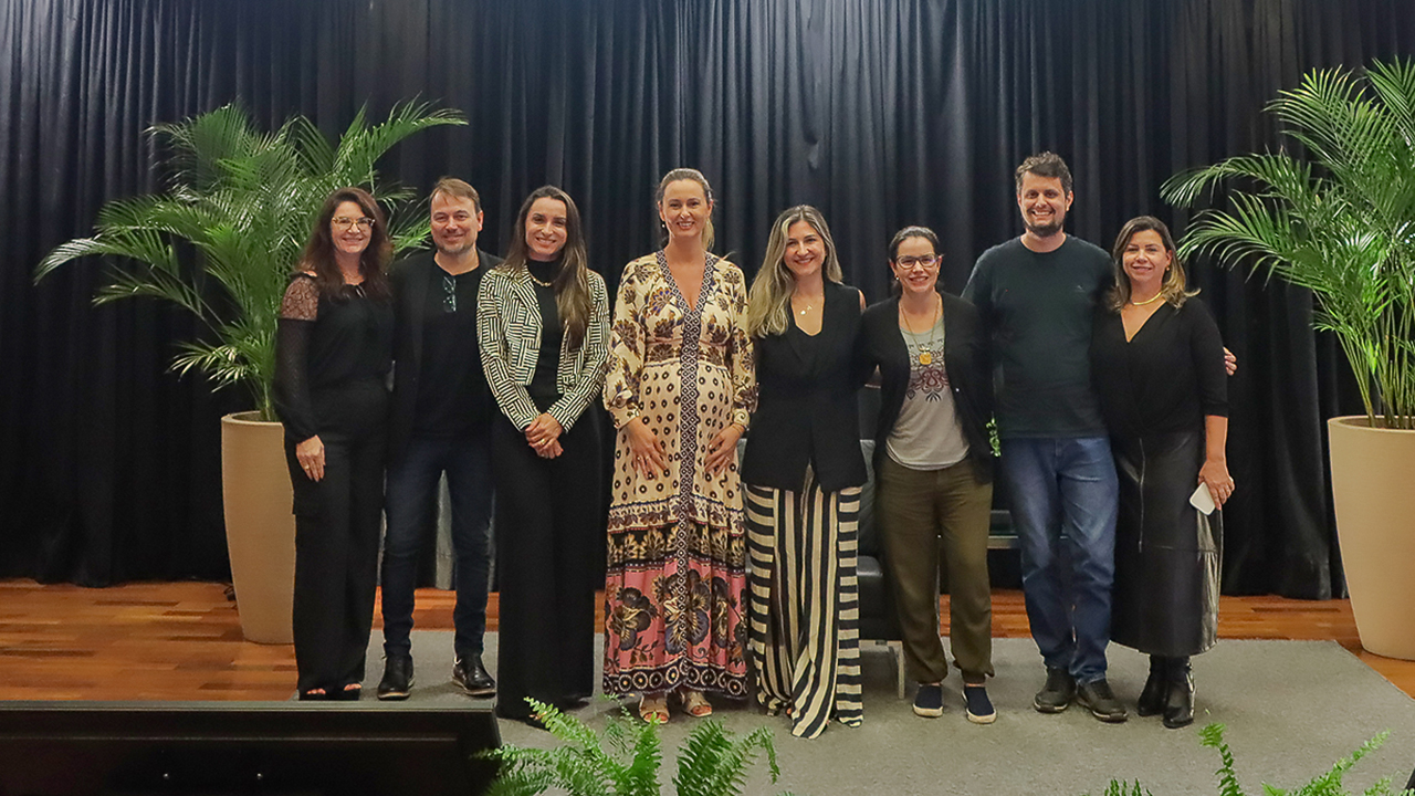 Banner horizontal com foto dos integrantes da Comissão ASG no palco do auditório do TCE/SC. Há oito pessoas, em pé, uma ao lado da outra. Ao centro, a coordenadora da comissão, Marina Ferraz de Miranda.