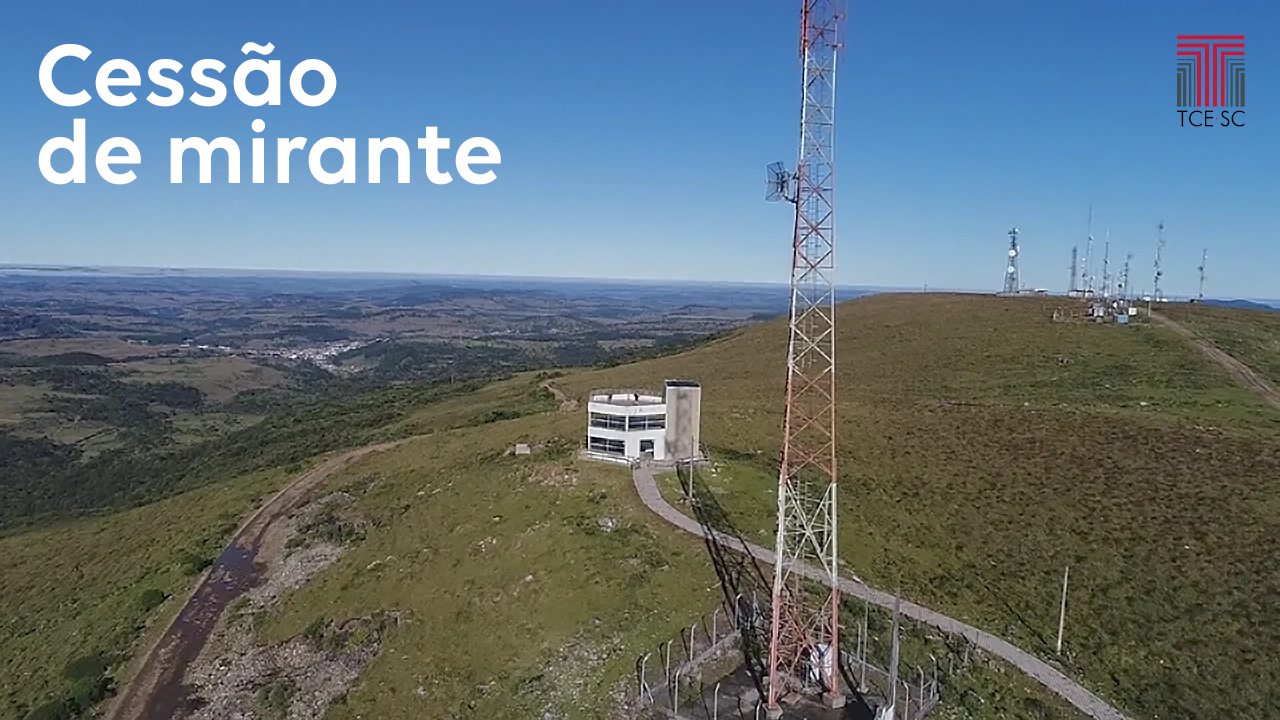 Imagem uma construção de dois andares ao centro. À direita dessa construção há uma torre. Ao fundo, também à direita, há mais algumas torres de transmissão. O cenário mostra o horizonte, com o céu azul e vegetação verde. Sobre o céu azul, escrito em branco, há à esquerda a expressão “Cessão de Mirante”. À direita, também sobre o céu azul, está o logotipo do TCE/SC