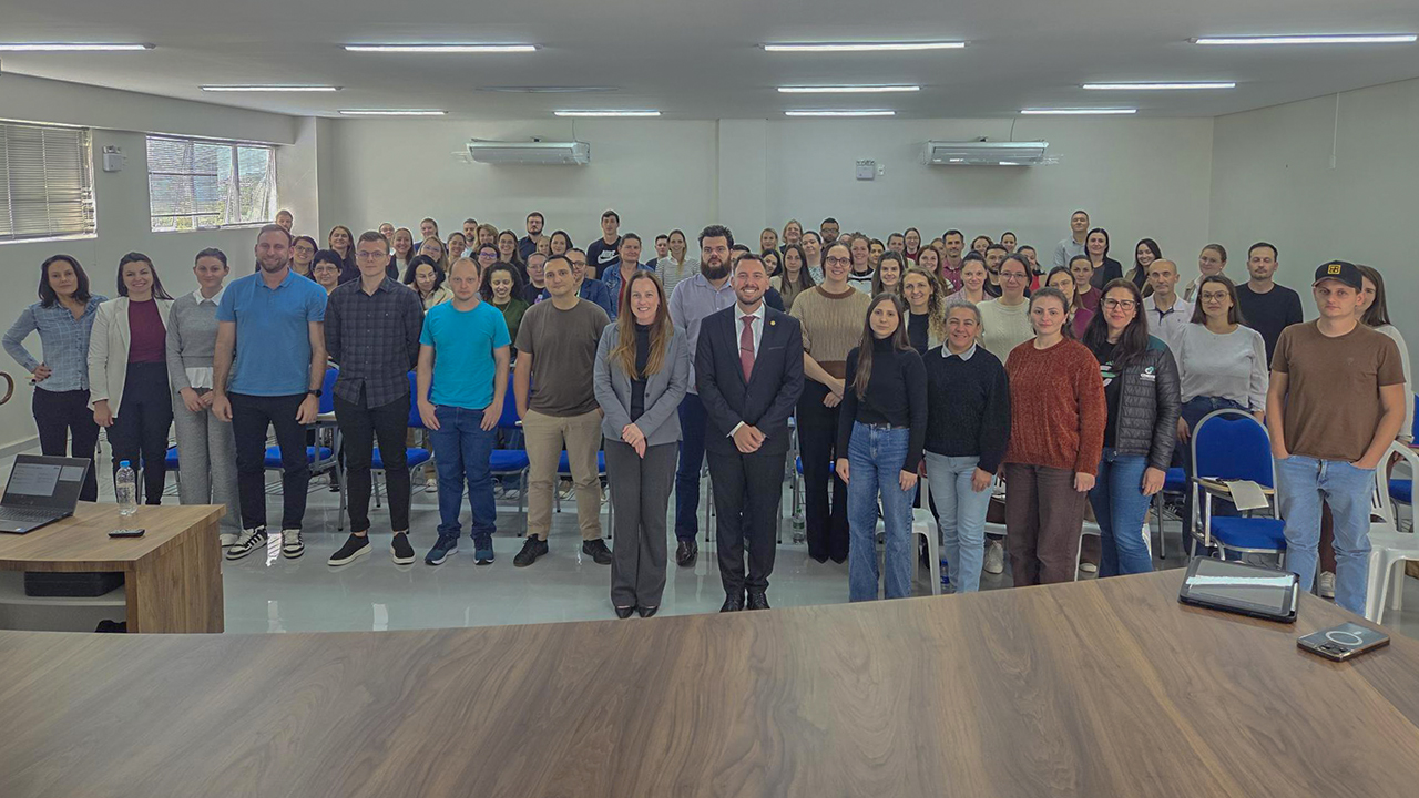 Banner horizontal com foto dos participantes da última etapa do Ciclo. Há várias pessoas, em pé, posicionadas lado a lado, em uma grande sala. Ao centro, os auditores Geovane Eziel e Vivan Savedra. 