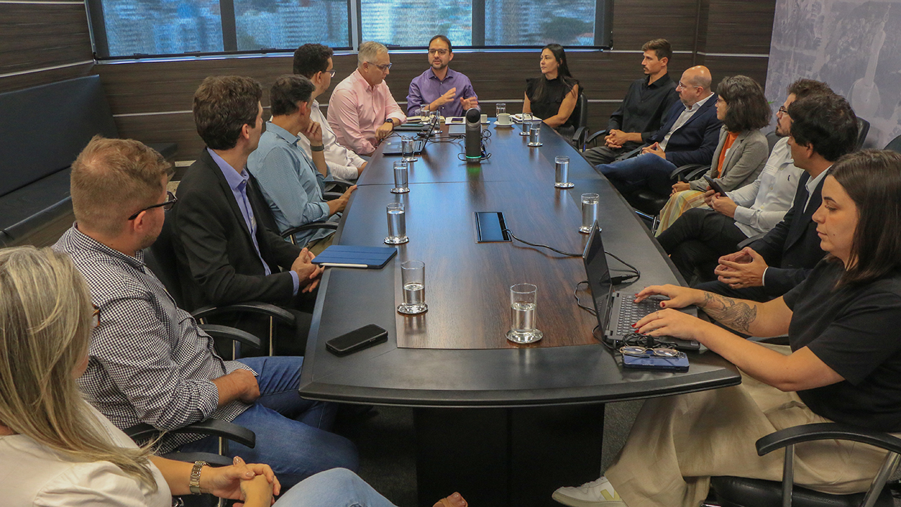 Foto que mostra 14 pessoas sentadas diante de uma mesa de reunião enquanto conversam, na sede do TCE/SC. Entre os presentes, integrantes da prefeitura de Florianópolis, do Todos pela Educação e do TCE/SC. Na ponta, o servidor Rafael Tachini e o diretor-geral de Controle Externo, Sidney Antônio Tavares Júnior. 