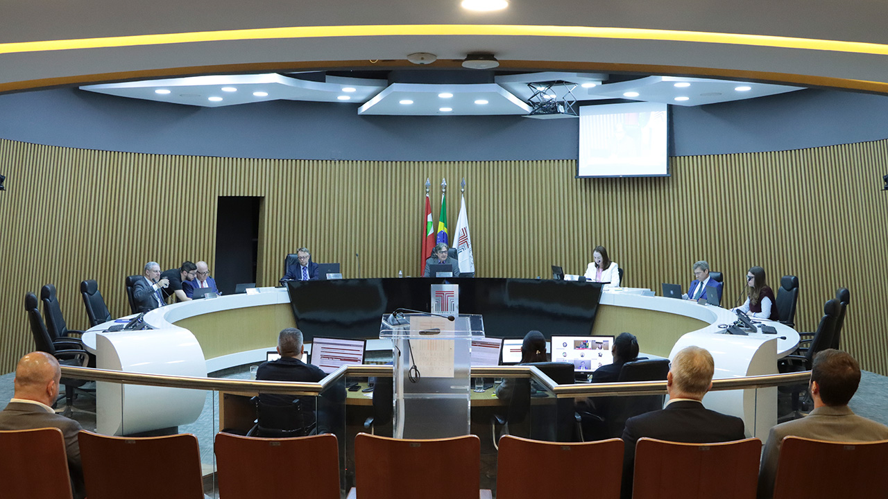 Banner horizontal com foto dos integrantes da Primeira Câmara no Plenário do TCE/SC. Ao centro da bancada circular, o presidente Aderson Flores. Ao redor, entre os presentes, os conselheiros Wilson Wan-Dall e José Nei Ascari, os conselheiros substitutos Gerson Sicca e Sabrina Iocken e o procurador Diogo Ringenberg. 