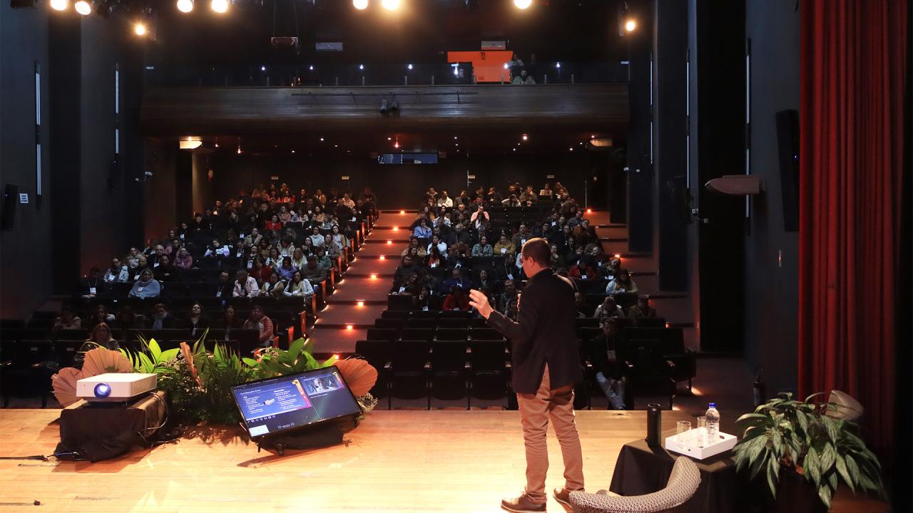 Banner horizontal com foto do diretor Nilsom Zanatto falando ao público. Ele está em pé, de costas, no palco do auditório. À frente dele, a plateia que participa do Ciclo. Há várias pessoas sentadas em poltronas, uma ao lado da outra. No palco, há plantas decorativas. 