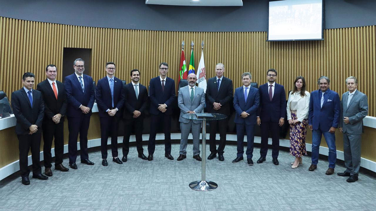 Banner horizontal com foto de autoridades reunidas no plenário do TCE/SC, com participantes da mesa de consensualismo e conselheiros alinhados lado a lado em frente a uma mesa central. Ao fundo, há painéis de madeira e bandeiras institucionais. No centro da imagem estão o defensor público-geral, Ronaldo Francisco, o secretário da Fazenda, Cleverson Siewert, o desembargador André Luiz Dacol e o presidente do TCE/SC, Herneus De Nadal, todos em trajes formais, posando para registro institucional.
