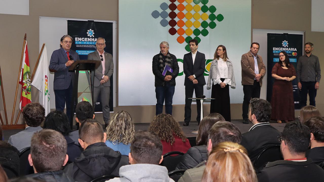 Banner horizontal com foto do evento em Lages. Na foto estão o conselheiro do TCE/SC Aderson Flores, o diretor-geral de controle externo Sidney Tavares Jr, o diretor da DLC Rogério Loch, a auditora fiscal Marina Casagrande, a serivdora Renata Ligocki Pedro, inspetor do Cres Edésio Alves Jr, representante do CREA James Clauberg e o diretor da Acil Alberto Engel. Eles estão no palco.