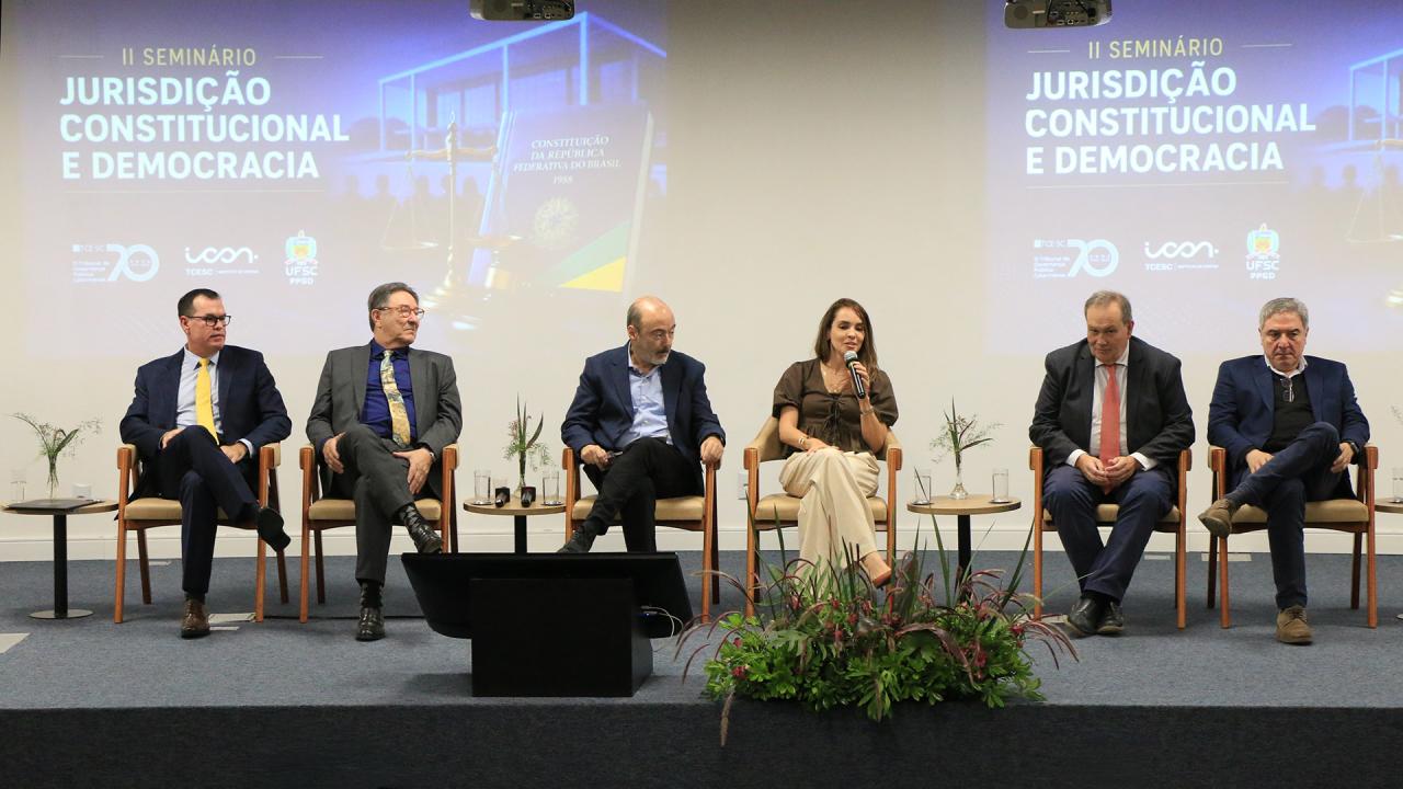 Banner horizontal com foto de seis autoridades sentadas em poltronas lado a lado no palco do auditório do TCE/SC. Entre os presentes, o corregedor-geral, conselheiro Adircélio Ferreira Júnior, e o professor Luiz Henrique Cademartori. O cenário tem plantas decorativas. Ao fundo, projeção de slides.