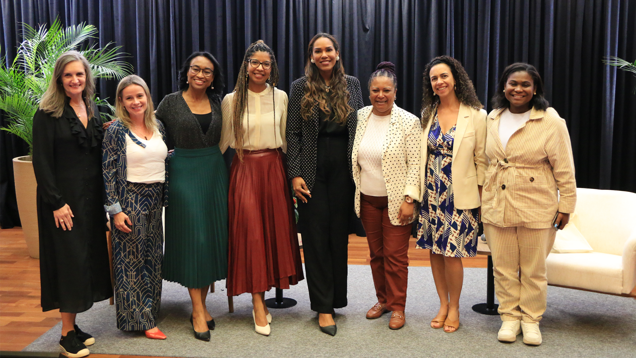 Banner horizontal com foto de oito mulheres no palco do auditório do TCE/SC durante o evento. Entre as presentes, as palestrantes, Marcela Timóteo, Clara Marinho, Daiesse Bomfim, Lorena Araújo e Lisiane Lemos, e a diretora do CTEDI, Walkiria Maciel. Elas estão lado a lado, posando para a foto.