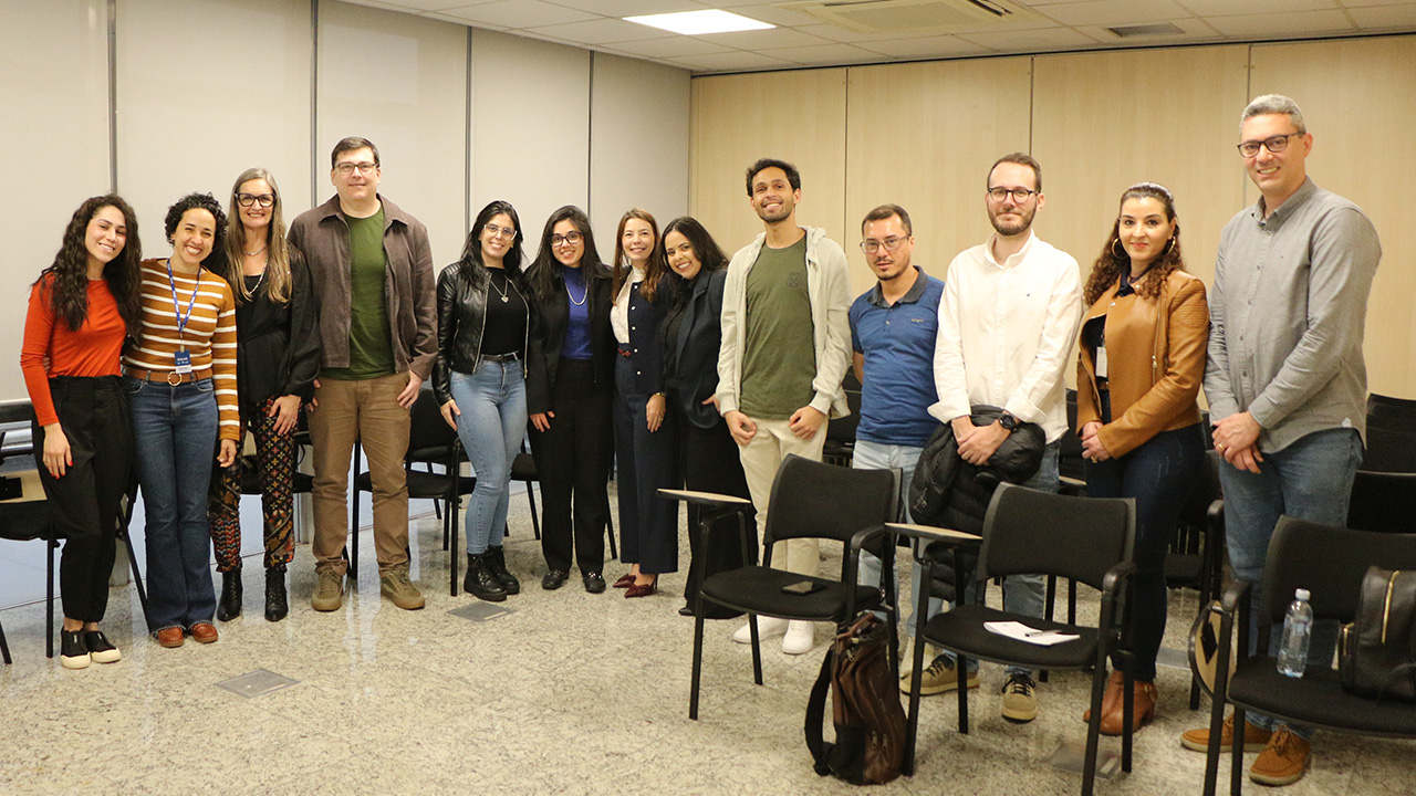 Foto horizontal com os novos residentes e com os integrantes da Diretoria de Gestão de Pessoas; ao todo, há 13 pessoas, sendo 8 mulheres e 5 homens, que estão em pé na sala de aula do Instituto de Contas 
