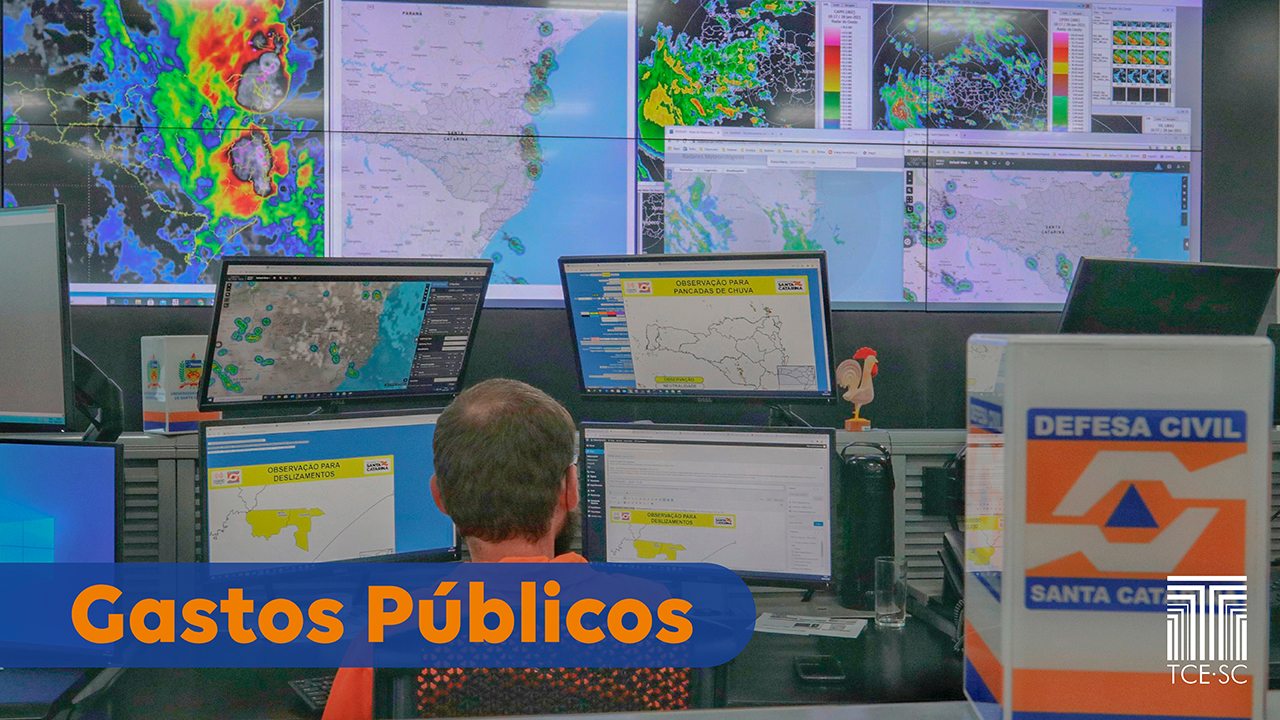 Foto de um técnico da Defesa Civil, de costas, na sala de controle, tendo, à sua frente, vários monitores mostrando mapas meteorológicos. À direita do técnico, há uma caixa com a logo da Defesa Civil de Santa Catarina. Na parte inferior esquerda há o título “Gastos públicos”, em fonte laranja sobre uma tarja azul. E no canto inferior direito, a logomarca do TCE/SC.  