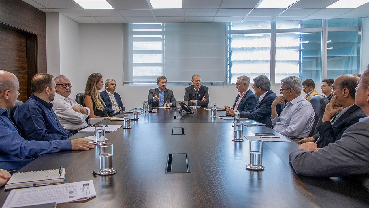 Banner horizontal com foto de reunião institucional entre integrantes do TCE/SC e representantes de agências reguladoras. Os participantes estão distribuídos nas laterais da mesa. Entre os presentes, os conselheiros Herneus De Nadal e José Nei Ascari, a coordenadora da relatoria temática, Ana Sophia Hillesheim, chefes de gabinete e demais integrantes do tribunal.   