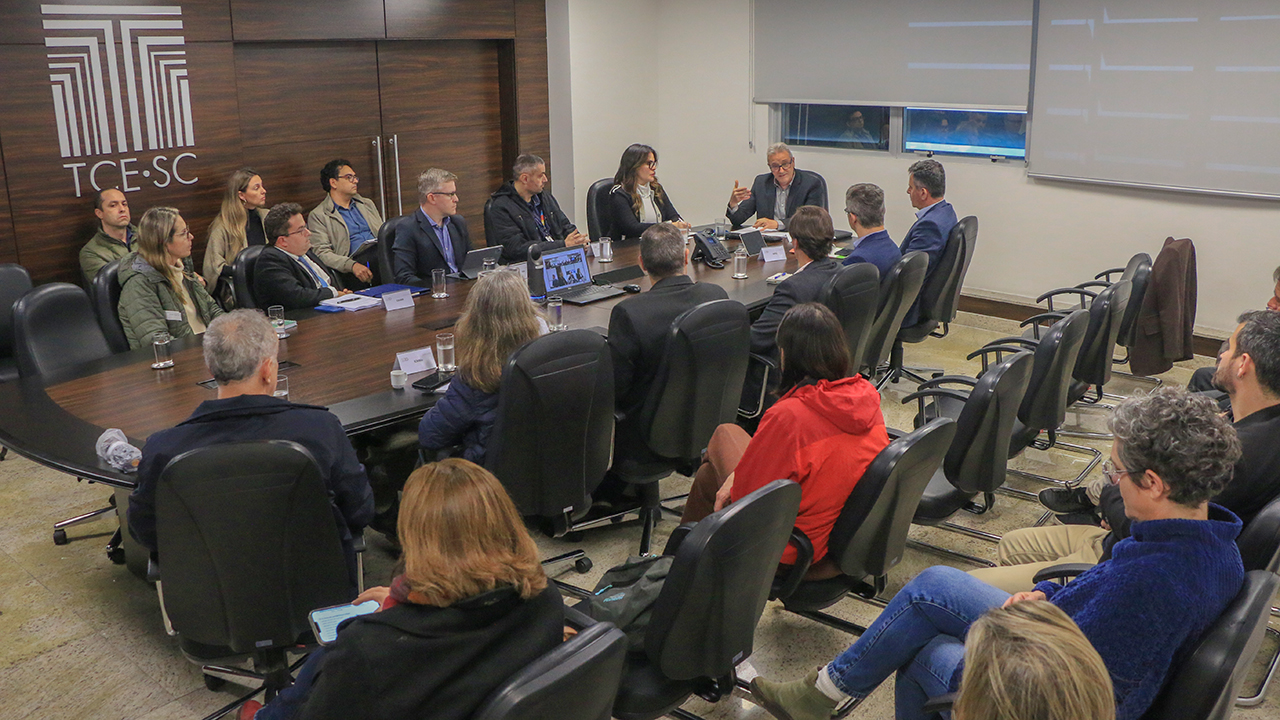 Banner horizontal com foto dos vários participantes da mesa de consensualismo reunidos no TCE/SC. Eles estão sentados diante de uma mesa, enquanto conversam. Entre os presentes, o coordenador dos trabalhos, Neimar Paludo, outros integrantes do TCE/SC, da Casan e de outras instituições envolvidas. 