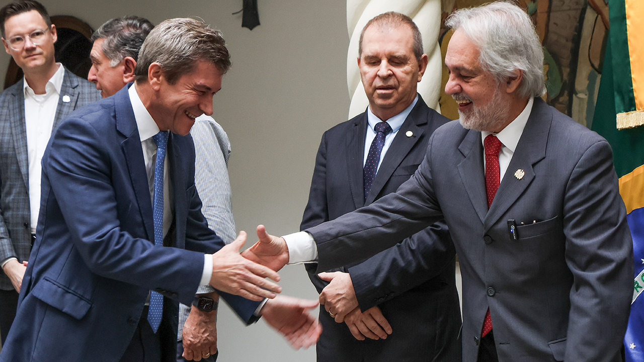 Em primeiro plano, o presidente em exercício do TCE/SC, conselheiro José Nei Ascari, aperta a mão do governador em exercício, João Henrique Blasi, sendo observador por um homem ao centro. 