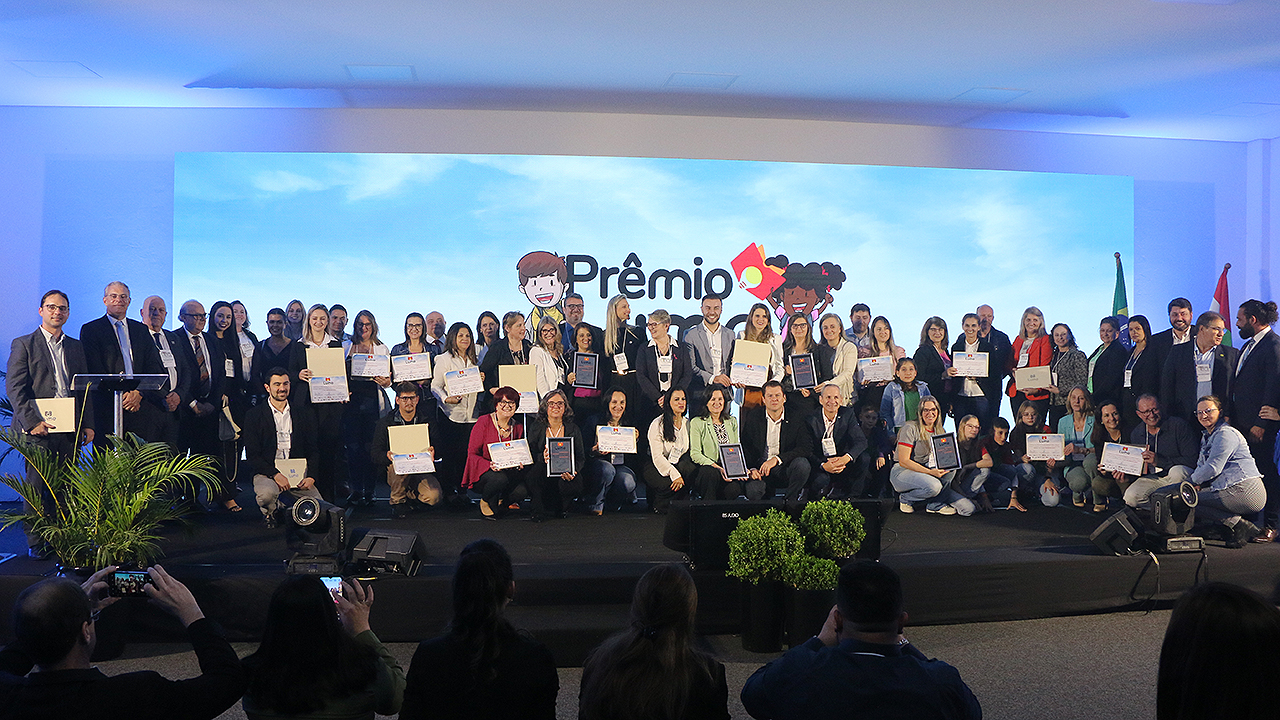 Imagem mostra todos os vencedores do Prêmio Lume no palco. Há cerca de 50 pessoas no palco. O fundo é azul.