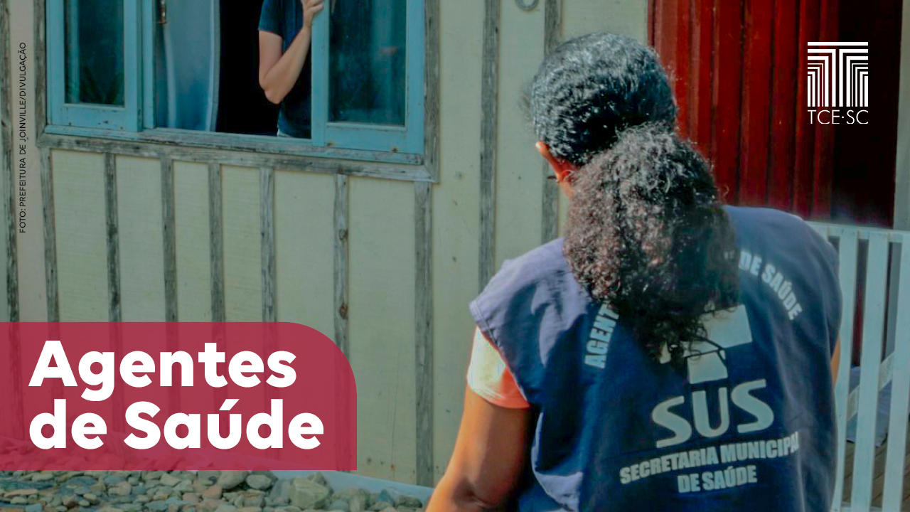 Imagem mostra foto de um agente de saúde em visita a uma casa. A gente aparece à direita na foto, de cabelo amarrado, vestindo um colete azul escuro onde se pode ler, em letras brancas, a identificação como agente e o logo do SUS. Ao fundo, em uma janela azul claro numa parede de madeira, aparece uma pessoa sem identificação