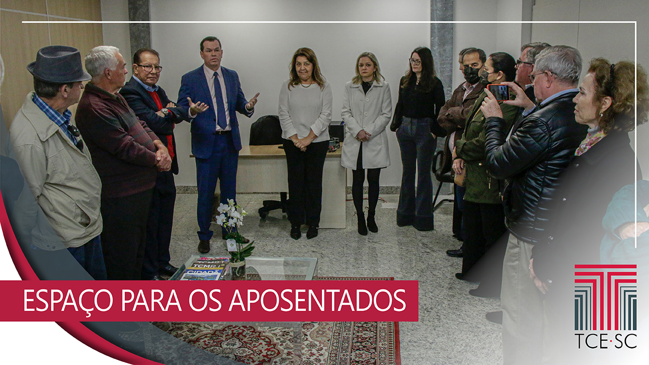 A imagem mostra um grupo de pessoas. Ao centro, a presidente da Associação dos Servidores Aposentados do TCE, Nair Passig. que veste uma blusa branca e calça preta. Ao lado esquerdo dela, conversando com os presentes, está o presidente do TCE/SC, conselheiro Adircélio de Moraes Ferreira júnior, que está de traje e grava azul. Ao lado direito de Nair está Juliana Cardoso, que é a chefe de gabinete da presidência, a diretoda de Gestão de Pessoas, Geani Fiorini, e o conselheiro aposentado Gilson dos Santos