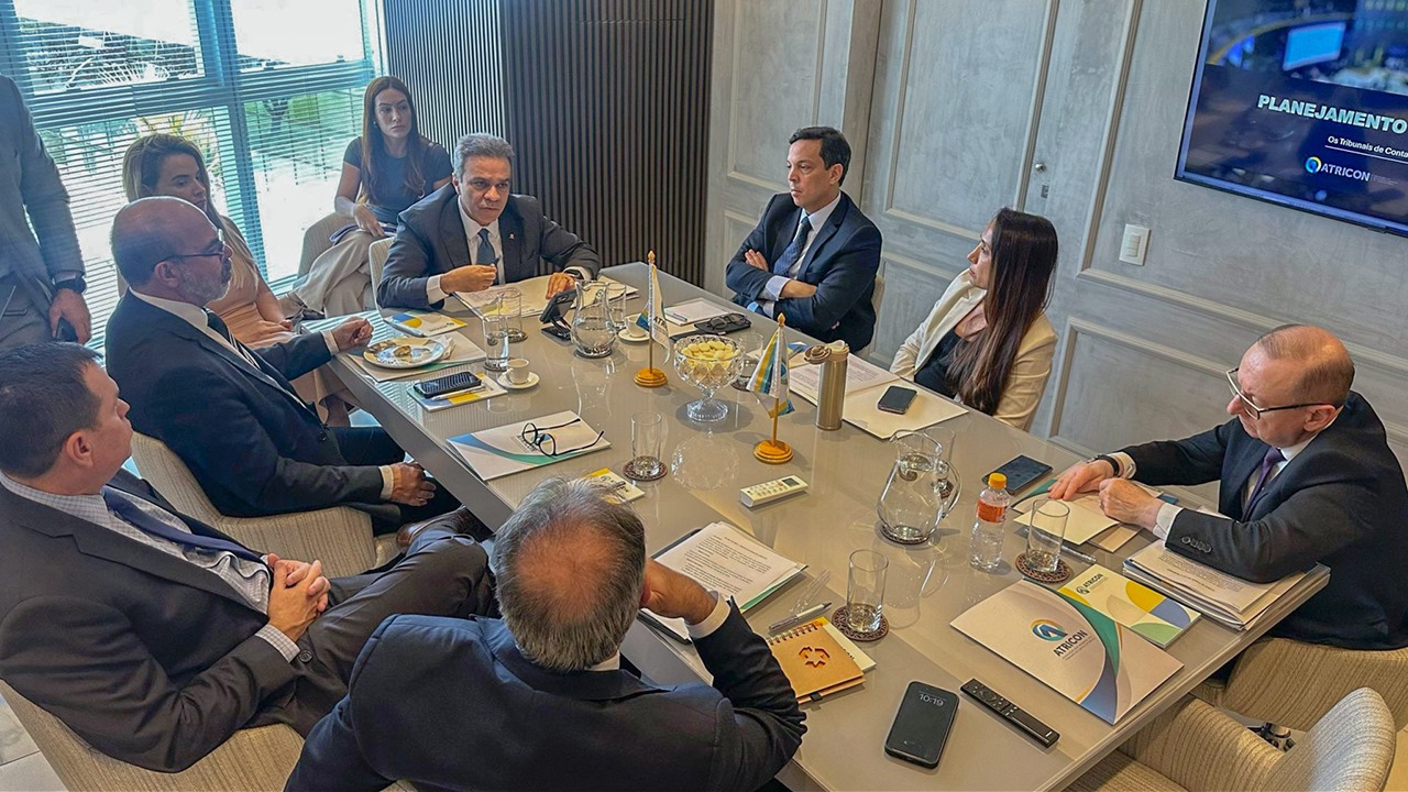 Foto mostra integrantes da Atricon sentados ao redor de uma mesa. Ao todo são nove pessoas, três delas mulheres. Ao fundo há uma janela por onde entra luz.   
