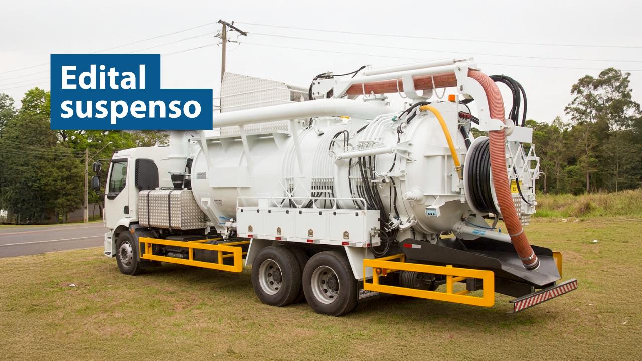 Banner horizontal com foto de um caminhão equipado com sistema de sucção e limpeza, com mangueiras e compartimentos acoplados na parte traseira, estacionado em área aberta com vegetação ao redor. No canto superior esquerdo, em tarjas azuis, o texto "Edital suspenso".