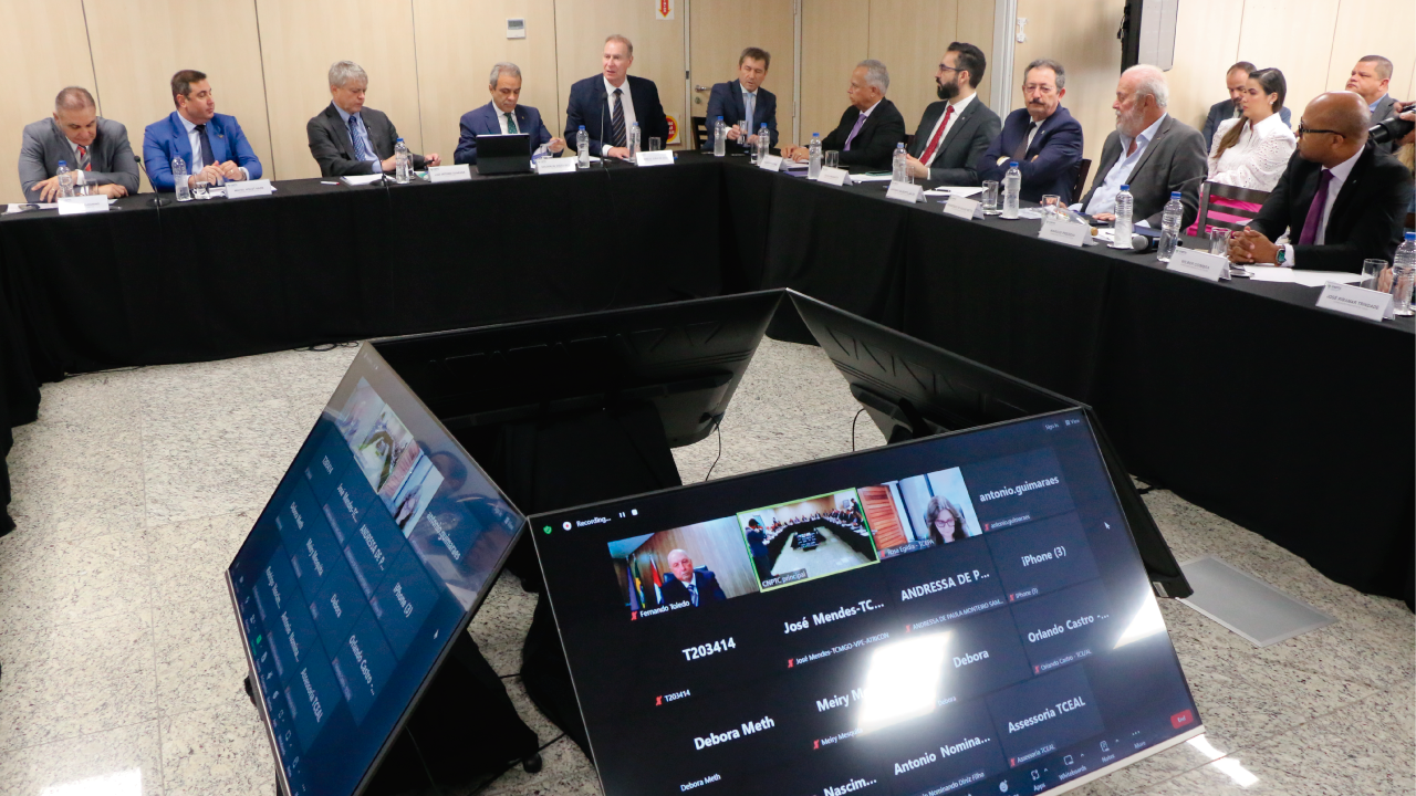 Foto da sala onde aconteceu a reunião. As mesas estão dispostas em formato de U, e ao centro, quatro monitores de televisão, voltados para cada lado da formação de mesas. Sentadas, estão vários presidentes. O presidente do TCE/SC, Herneus de Nadal, aparece ao lado do presidente da Atricon, Edilson Silva. Entre outros conselheiros aparece o vice-presidente do TCE/SC, José Nei Ascari.