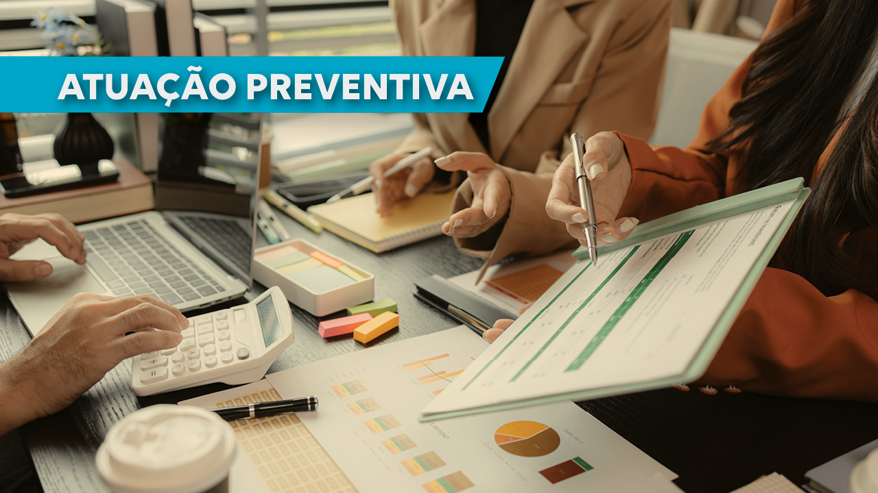 Imagem mostra uma mesa com pessoas trabalhando ao redor, sem aparecer os rostos. Uma pessoa manuseia uma calculadora, a outra mostra uma planilha e uma terceira está apontando para essa planilha. No alto, à esquerda, escrito em branco no fundo azul, está escrito Atuação Preventiva