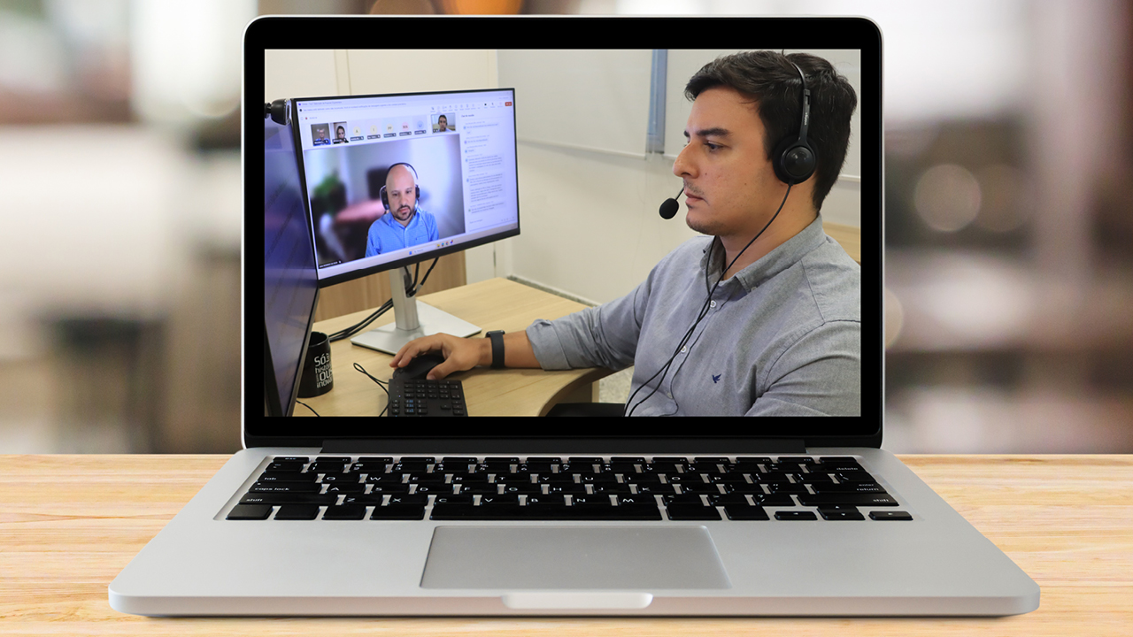 Banner horizontal com imagem de um notebook aberto sobre uma mesa. Na tela, aparecem os auditores Leonardo Favaretto e Jean da Silva durante a capacitação on-line. Eles usam fones de ouvido e mexem no computador. 