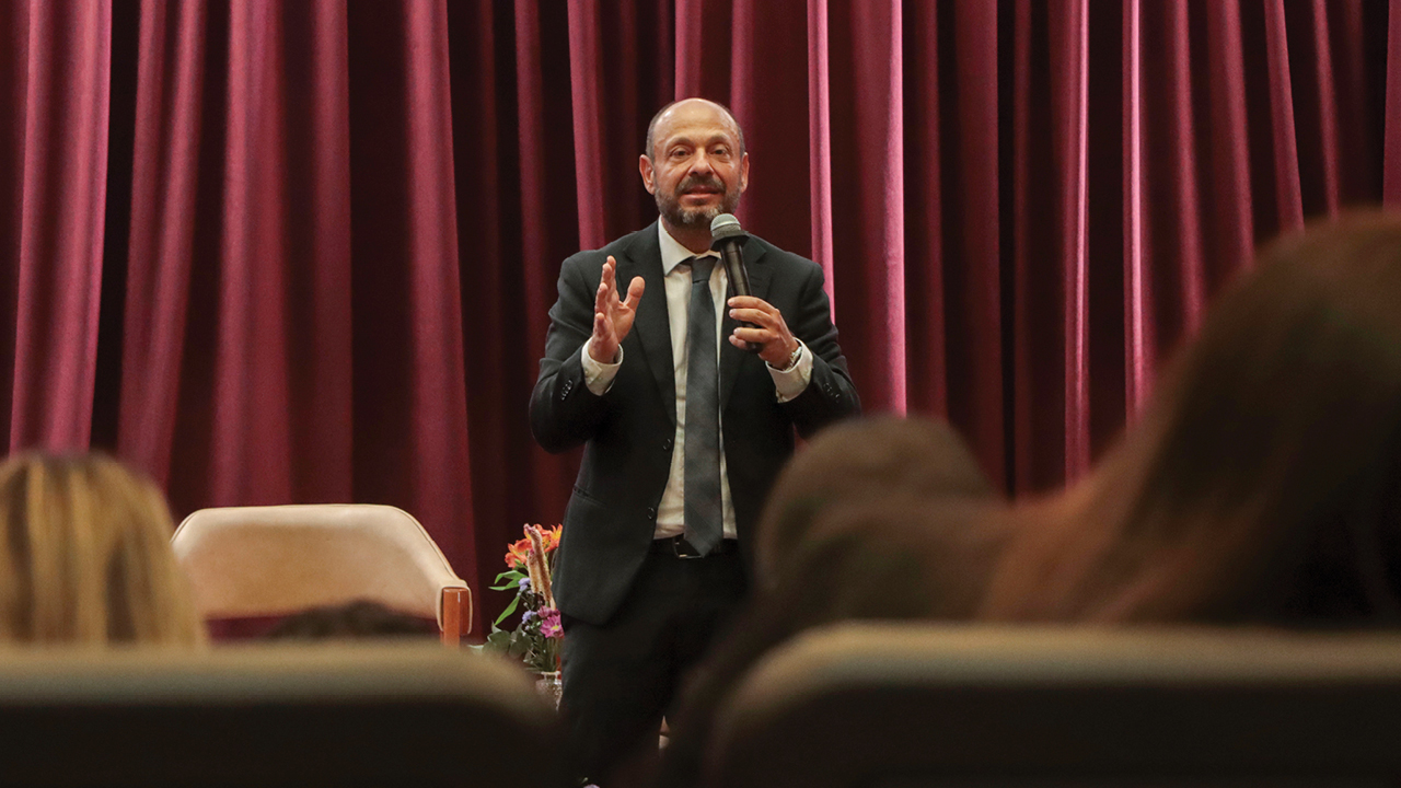 Banner horizontal com foto do procurador federal Gilberto Waller Júnior falando ao público em evento no auditório. Ele é um homem branco, de barba grisalha. Veste terno e gravata e está em pé, no palco. Ao fundo, há cortinas bordôs compondo o cenário. À frente dele, em primeiro plano e de costas, algumas pessoas na plateia.