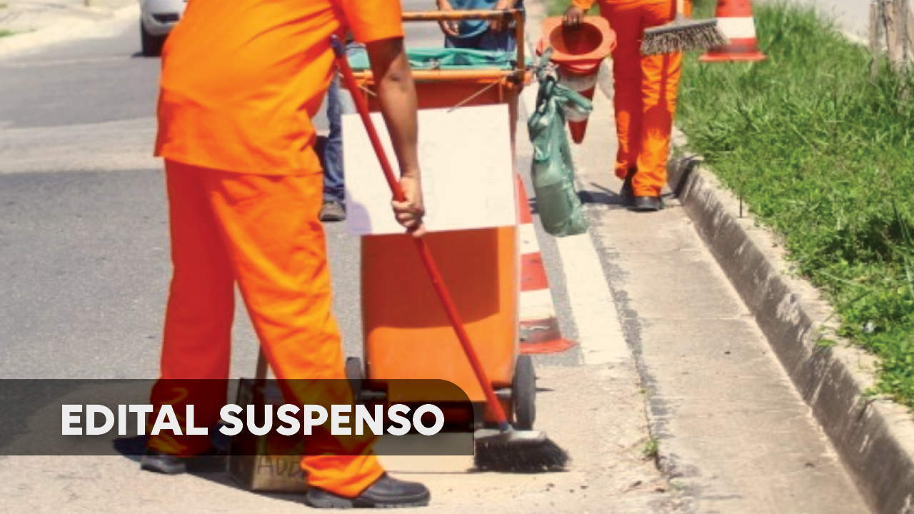Foto de um gari, de costas, com macacão alaranjado, segurando uma vassoura, varrendo a rua, próximo ao meio fio. A sua frente, um coletor de lixo, alaranjado. A foto está cortada na altura dos ombros, de modo que não aparece a cabeça do gari. No canto inferior esquerdo, uma tarja escura, com o título “Edital suspenso”. 