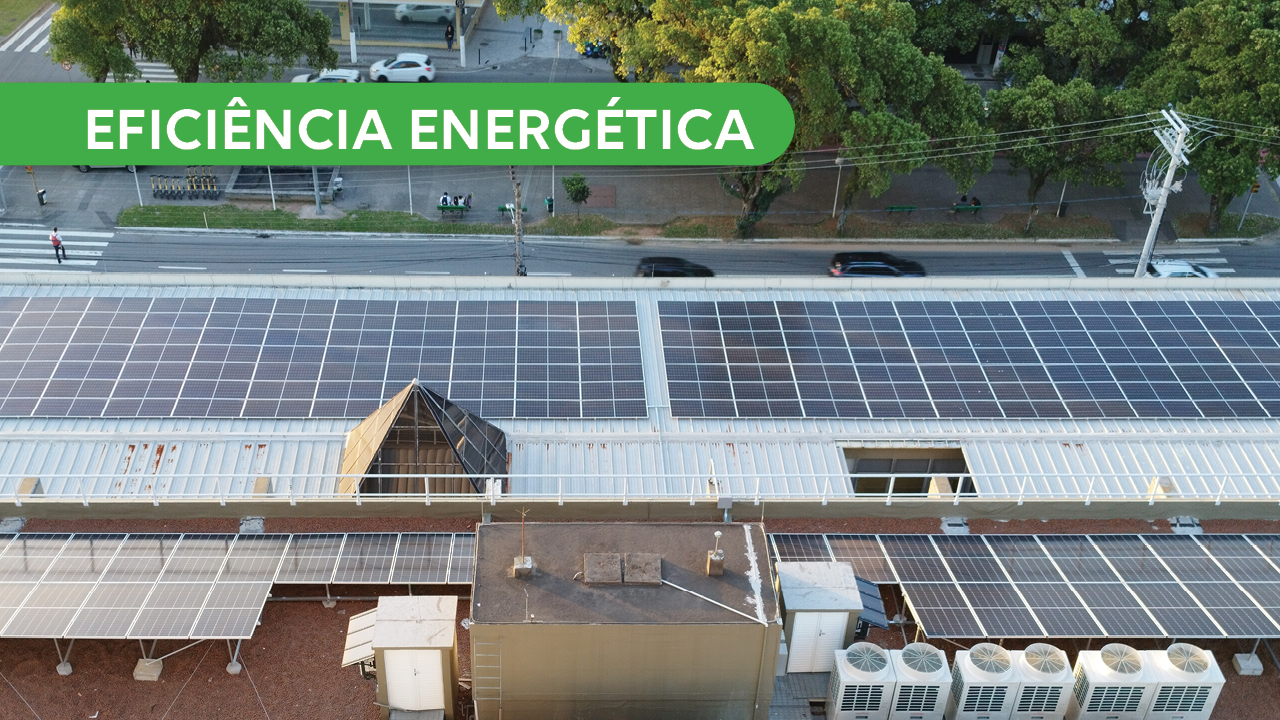 Foto das placas de energia solar, do ponto de vista de um andar alto do prédio do TCE/SC. No canto superior esquerda, sob fundo verde e letras brancas, está a expressão "Eficiência Energética".