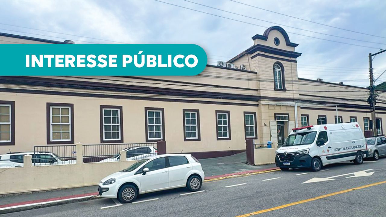 Banner horizontal com foto da fachada do Hospital da Polícia Militar Lara Ribas. É uma construção com arquitetura antiga, com paredes bege, detalhes em marrom, diversas janelas e uma torre central com janela em arco. Em frente ao edifício, na rua, há um carro branco estacionado e uma ambulância. Sobre a foto, em tarja verde-água, o texto "Interesse público".