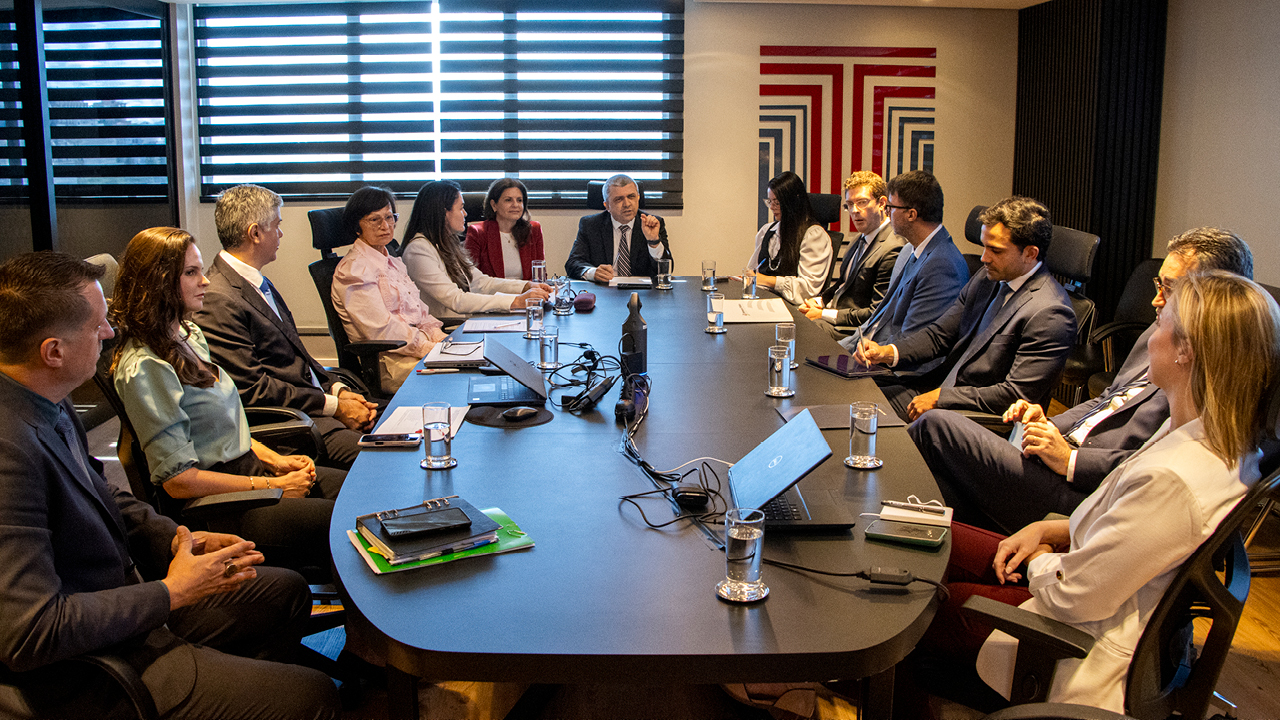  Foto horizontal que mostra os participantes da reunião. Há várias pessoas sentadas diante de uma mesa, enquanto conversam. Entre os presentes, o coordenador da mesa, Márcio de Medeiros, e a diretora-geral adjunta de Controle Externo Monique Portella, além de outros integrantes do TCE/SC e das demais instituições. Na parede, ao fundo, plotagem com logo do Tribunal.
