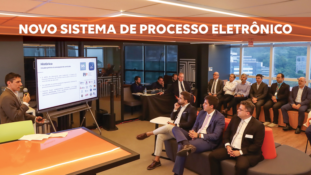 Banner horizontal com foto da reunião de apresentação. À esquerda, falando ao microfone, o diretor Rafael Gonçalves, fazendo a apresentação. À direita, sentados em poltronas, um ao lado do outro, os participantes que assistem. Entre eles, o presidente Herneus De Nadal. Sobre a foto, na parte superior, em tarja laranja, o título “Novo sistema de Processo Eletrônico”. 