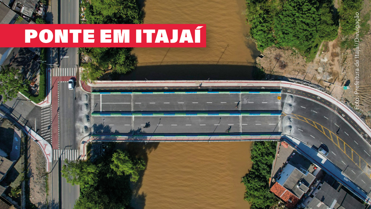 A imagem mostra uma ponte vista de cima, sobre um rio barrento. A ponte tem quatro pistas. Na parte alta da imagem ainda há uma ciclovia, inexistente na parte baixa. No alto, à esquerda, a expressão Ponte em Itajaí.