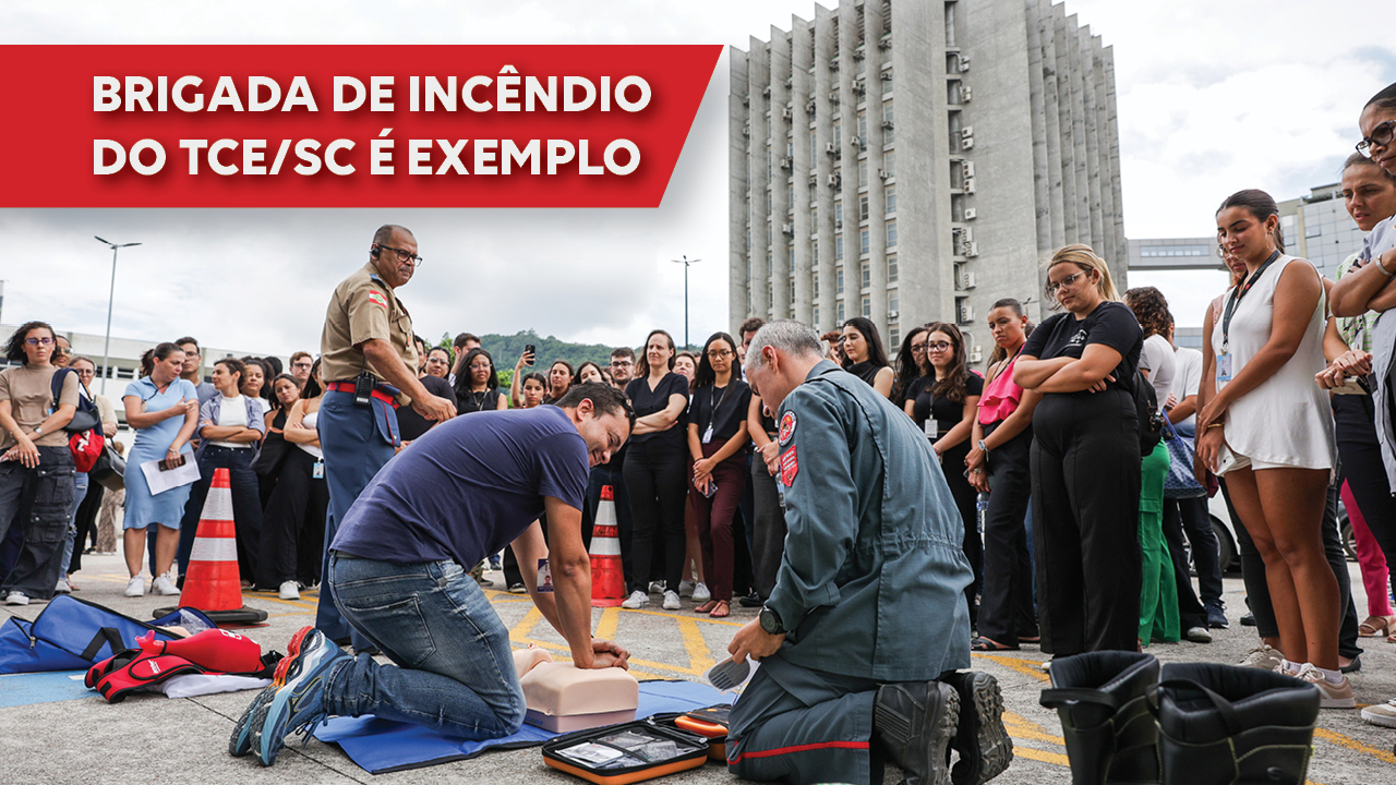 Imagem que mostra simulação de emergência em frente ao Fórum Rid Silva. Há várias pessoas olhando os brigadistas simulando uma massagem cardíaca. Atrás, é possível ver o prédio do Tribunal de Justiça. Sobre a foto, em retângulo bordô, o texto “Brigada de incêndio do TCE/SC é exemplo”.
