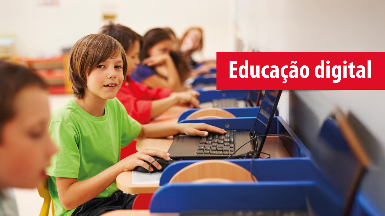 Banner horizontal com foto de várias crianças sentadas, lado a lado, em frente a um notebook. Há destaque para um menino que olha para a foto. Ele veste camiseta verde. Sobre a foto, na lateral direita, o texto "Educação digital", sobre tarja vermelha.