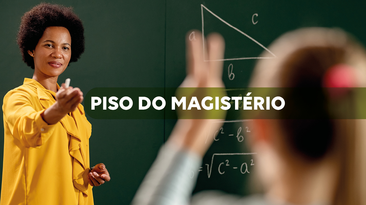 Banner horizontal com foto de uma professora em sala de aula, diante de um quadro verde com fórmulas matemáticas, enquanto uma aluna, em primeiro plano, levanta a mão. Ao centro, sobre uma faixa translúcida em verde-escuro, aparece o texto “Piso do magistério”, em branco.