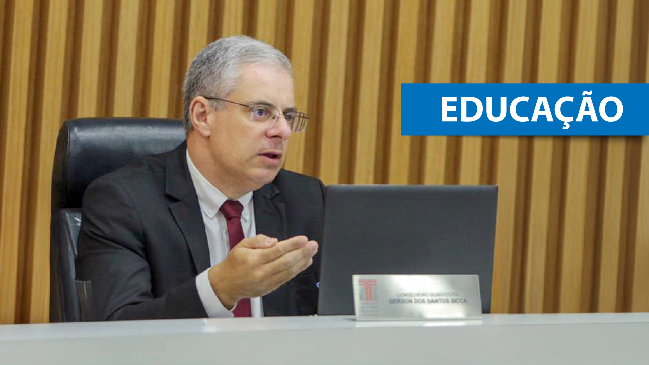 Foto do conselheiro substituto Gerson Sicca no plenário do TCE/SC. Ele é um homem branco, de cabelos grisalhos. Veste terno e gravata e está falando ao microfone. Sobre a foto, na lateral direita, em tarja azul, o texto “Educação”. 