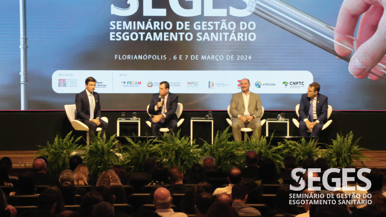 Foto dos quatro participantes do painel durante o Seminário. Da esquerda para a direita, o presidente da Fecam, Fabrício Oliveira, o conselheiro Adircélio de Moraes, o deputado Mauro de Nadal e o deputado federal Ricardo Zanatta Guidi. Ambos estão sentados em poltronas, no palco do auditório do evento, enquanto debatem. Ao fundo, projeção do logo do Seges no telão. 