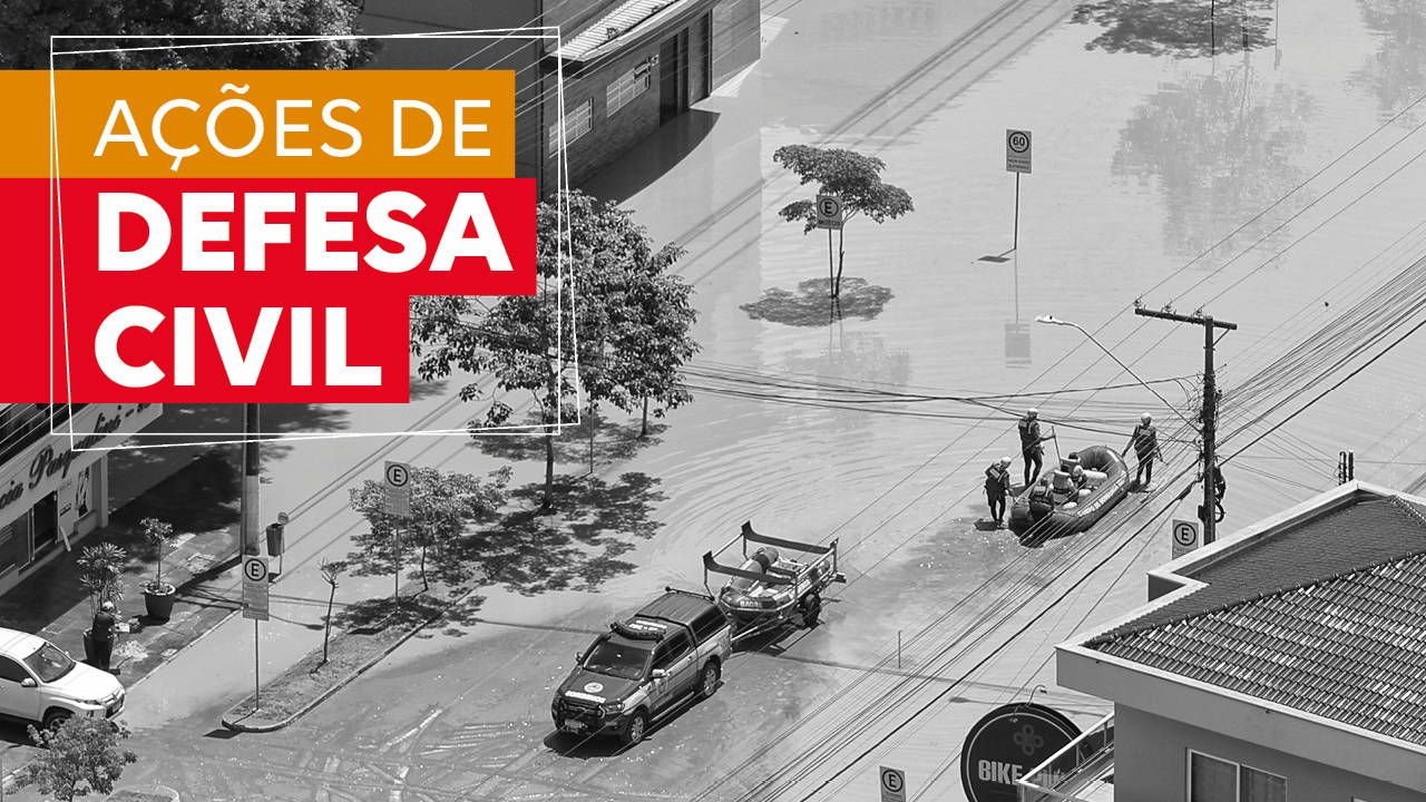 Banner horizontal com imagem aérea, em preto e branco, de um bote salva-vidas entrando em uma rua alagada, sendo puxado por profissionais de resgate. No canto superior esquerdo, sobre tarjas laranja e vermelha, o texto “Ações de Defesa Civil”.  