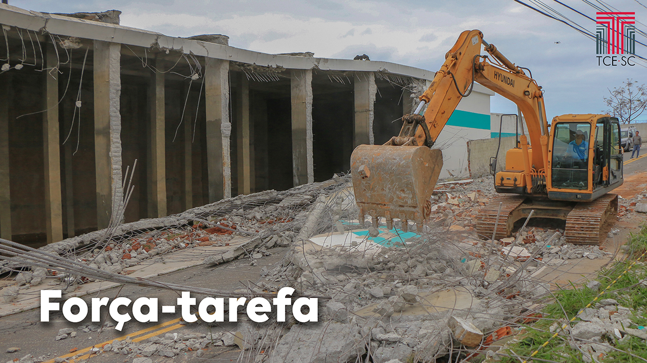 Foto dos escombros do reservatório de água da Casan, e de uma retroescavadeira fazendo a limpeza, retirando material do meio da rua. Na parte inferior direita da foto há o texto “Força-tarefa” e no canto superior direito há a logo do TCE/SC.