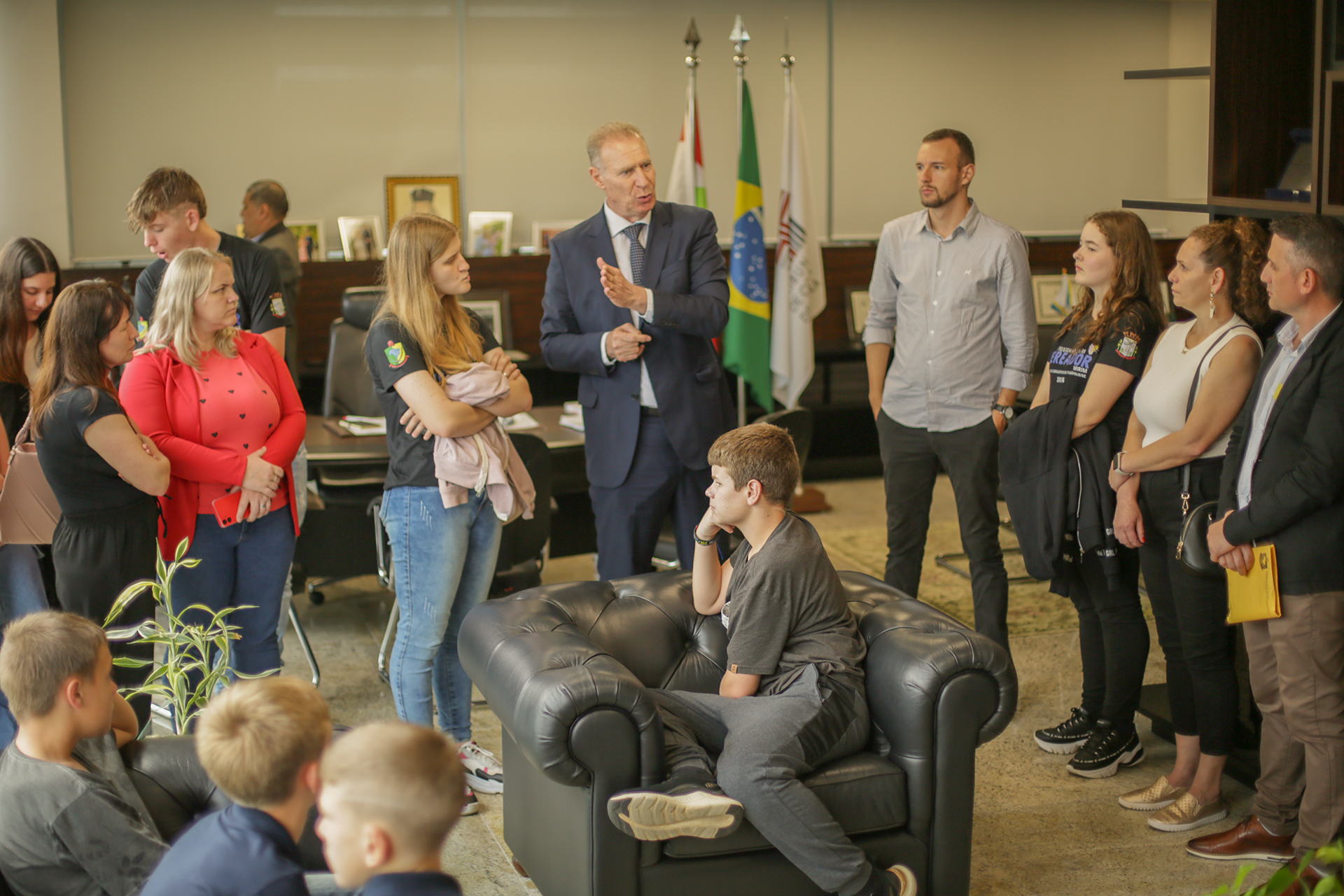 Foto de várias pessoas em uma sala do Tribunal durante visita dos vereadores mirins. O presidente Herneus De Nadal está ao centro, falando com as crianças e adolescentes. 