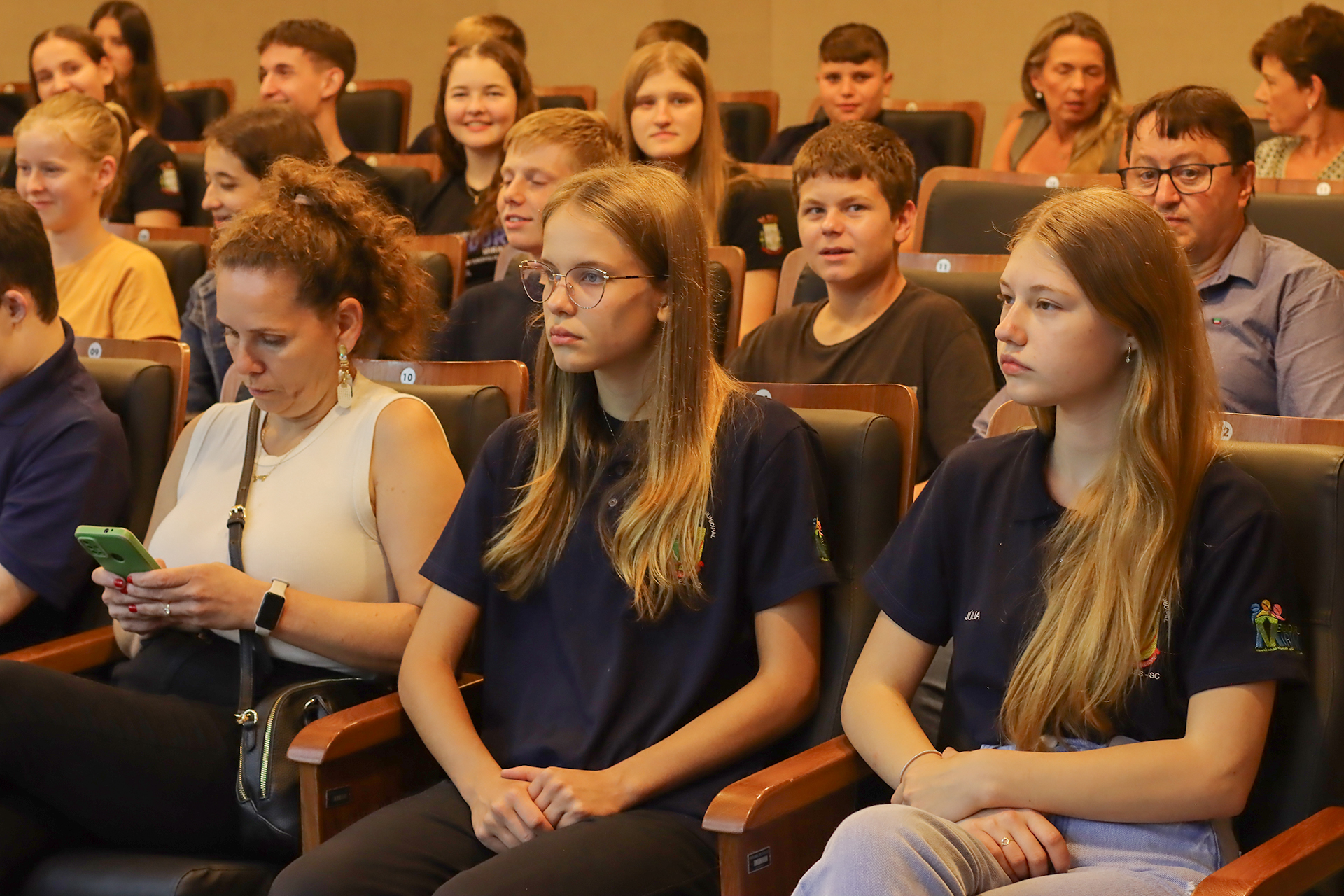 Foto dos vereadores mirins acompanhando a sessão plenária. Há várias crianças e adolescentes sentados em cadeiras no plenário do TCE/SC. 