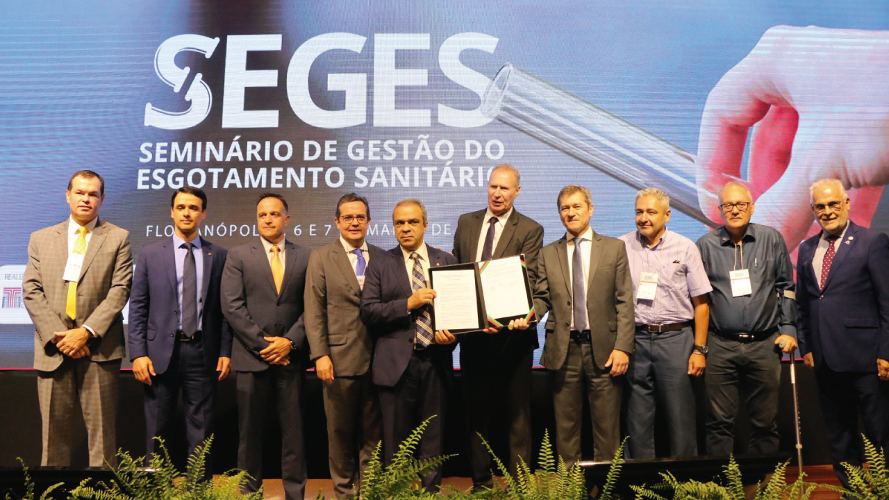 Foto das autoridades que assinaram o protocolo de intenções. Elas estão em pé, em frente ao telão com a projeção do logo do Seges. 