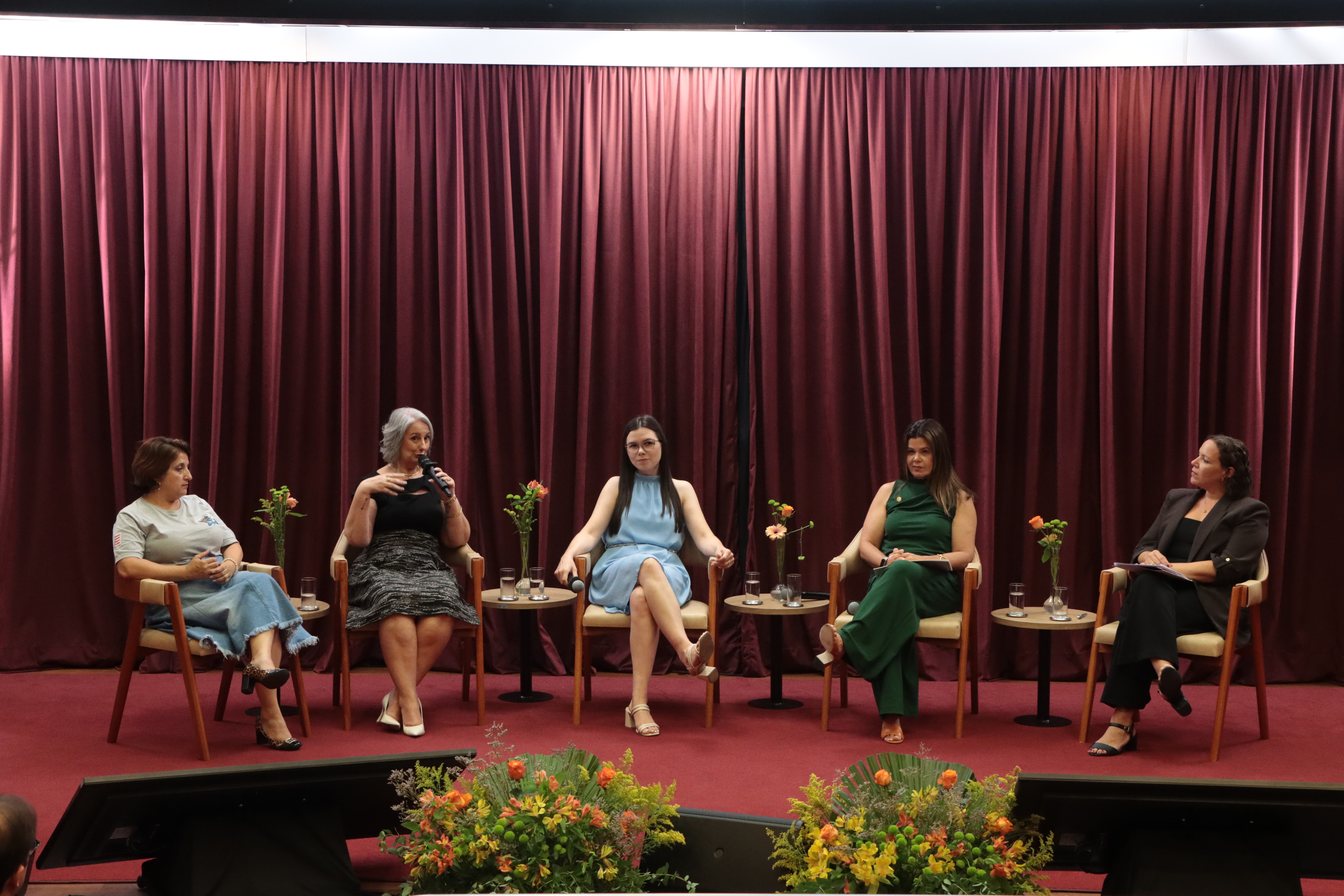 Foto de cinco mulheres no palco participam de uma mesa de debate sobre educação.