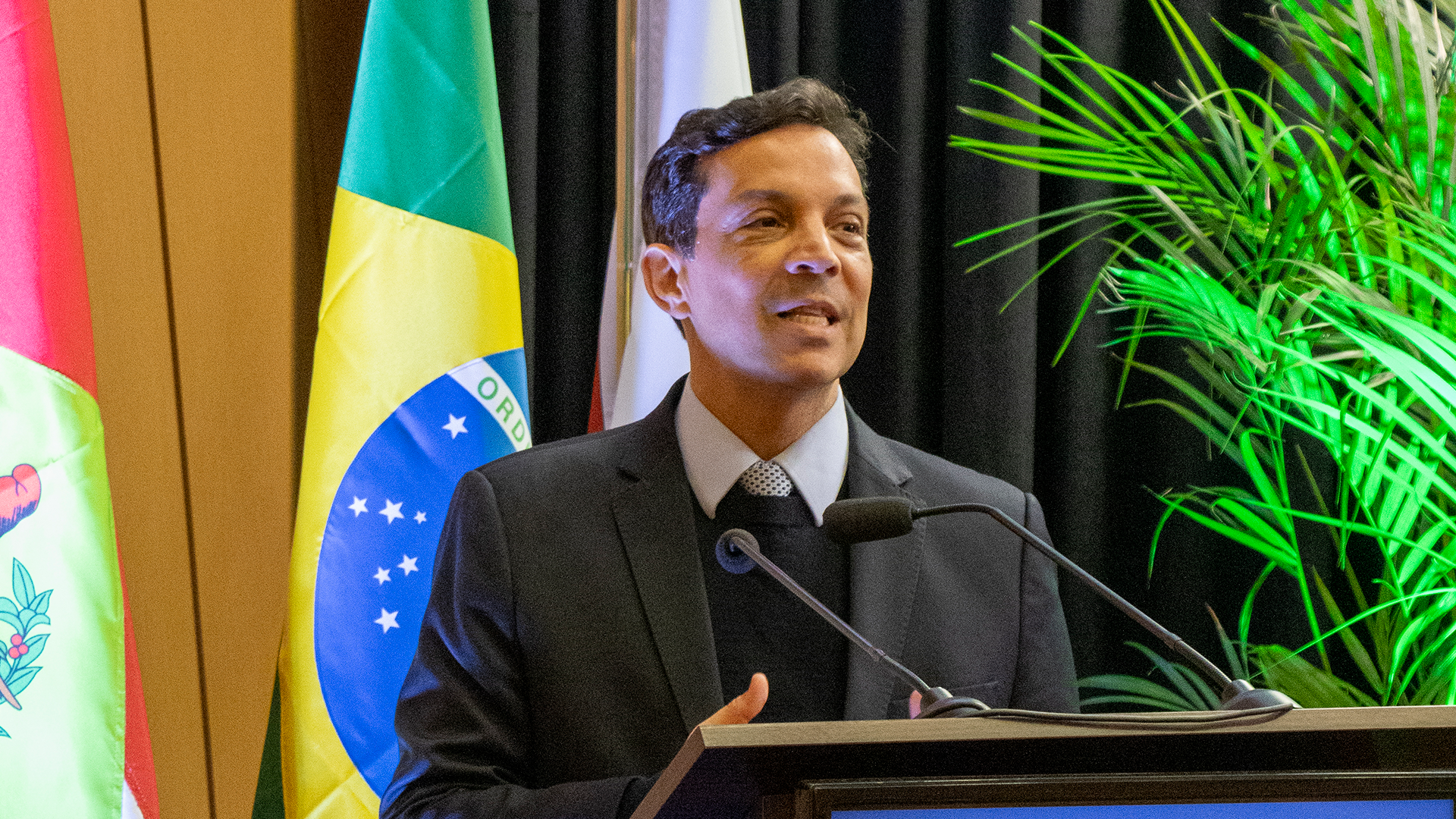Foto horizontal que mostra o conselheiro Carlos da Costa Pinto Neves Filho falando ao púlpito, na abertura do evento. Ao lado dele, demais autoridades presentes, no palco do auditório.