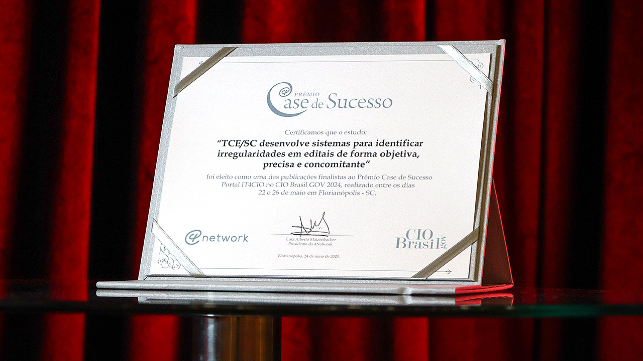 Banner horizontal com foto do certificado do estudo “TCE/SC desenvolve sistemas para identificar irregularidades em editais, de forma objetiva, precisa e concomitante” como um dos finalistas do prêmio case de sucesso sobre uma mesa de vidro. Ao fundo, uma cortina bordô. 