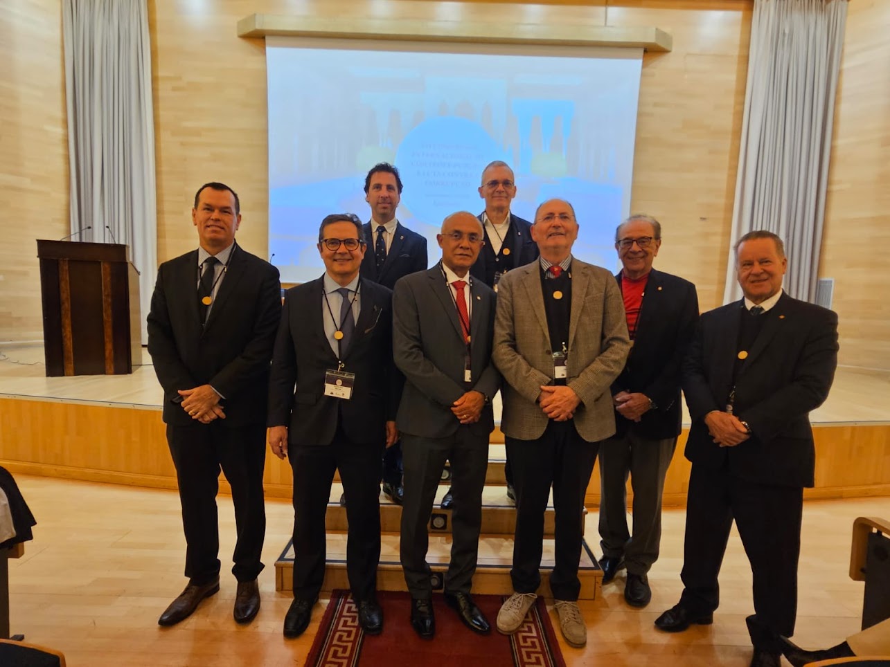 Foto horizontal de oito autoridades, lado a lado, em um ambiente interno, durante o evento internacional. Todos usam terno e gravata e medalhas institucionais. Entre os presentes, o conselheiro Adircélio de Moraes Ferreira Júnior e os integrantes do IRB Inaldo Araújo, Edilberto Carlos Pontes Lima e Sebastião Helvécio. 